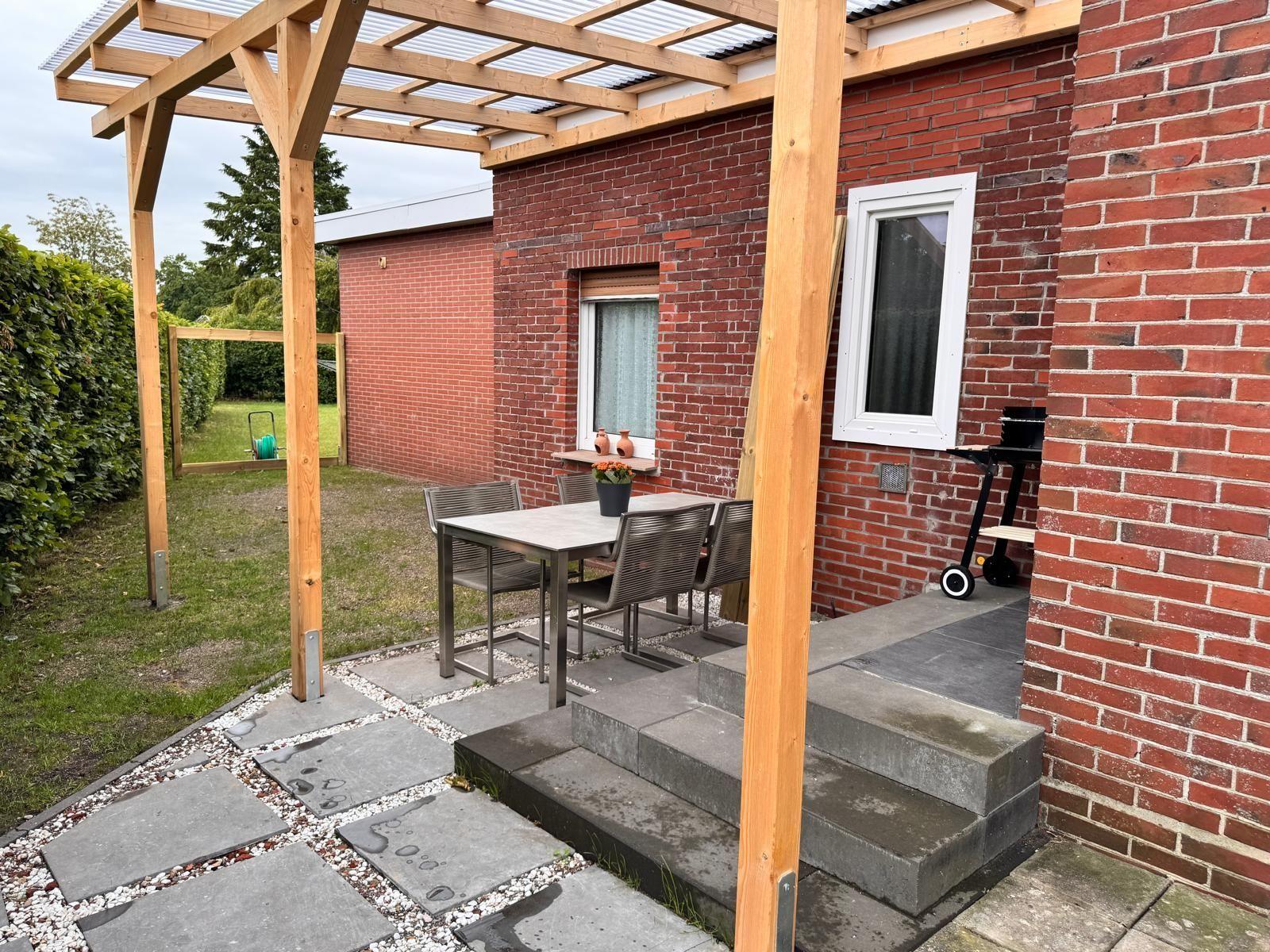 Terrasse mit Tisch, Stühlen und Grill neben rotem Backsteinhaus.