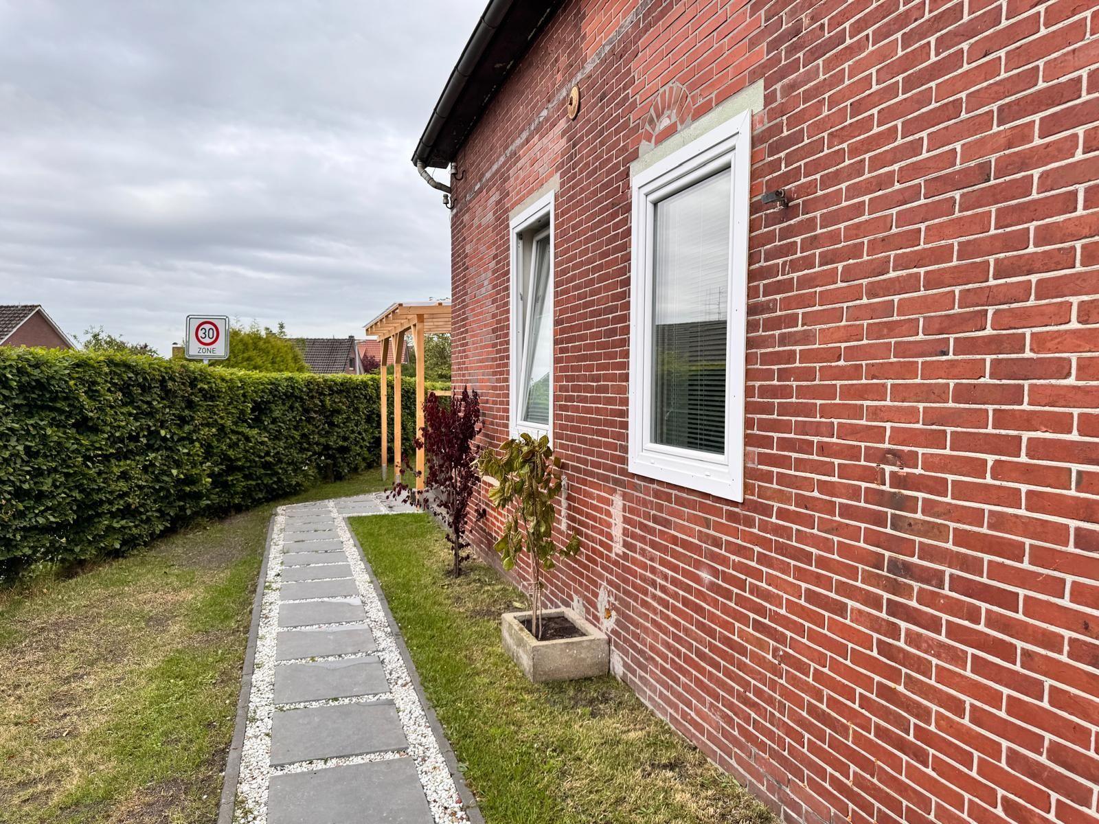 Rotes Backsteinhaus mit Gartenweg und Hecke. Fenster mit weißen Rahmen.