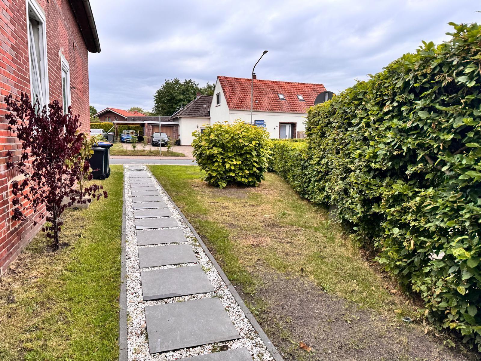 Gartenweg mit Steinen und Kies zwischen Rasen und Hecke.