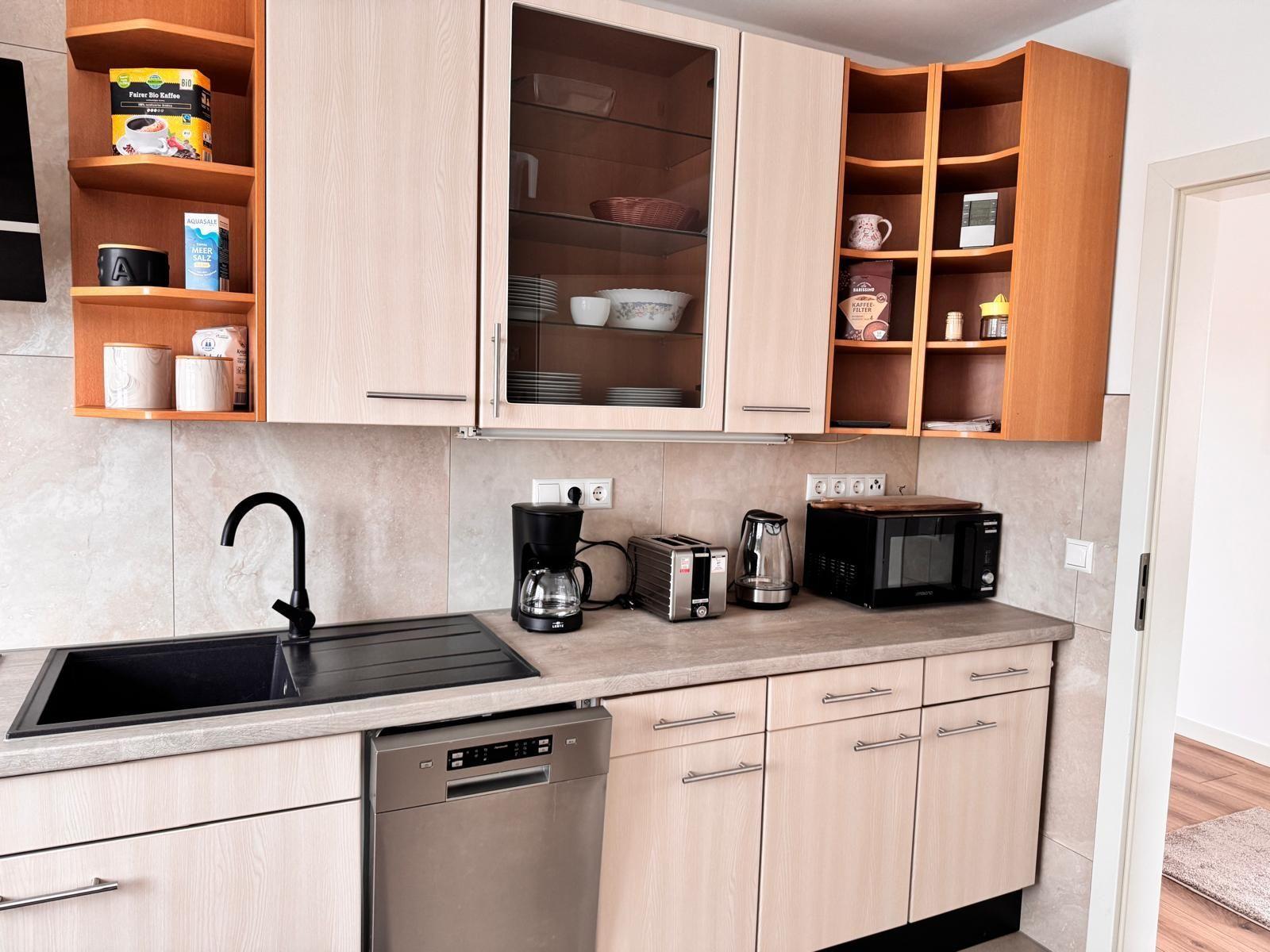 Küche mit Spüle, Kaffeemaschine, Toaster, Mikrowelle und Geschirr.