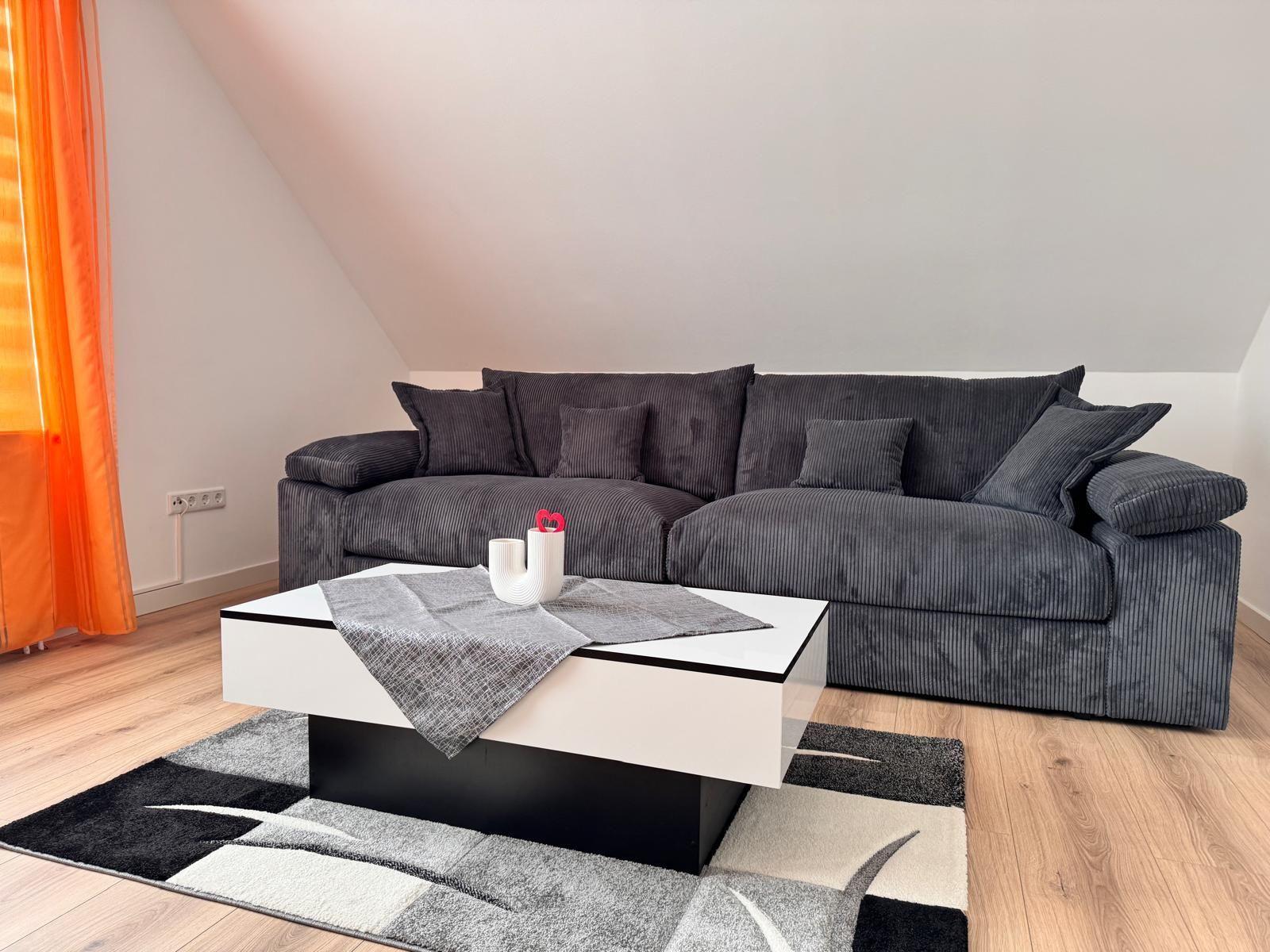 Ein Wohnzimmer mit grauem Sofa, weißem Couchtisch und Holzboden.