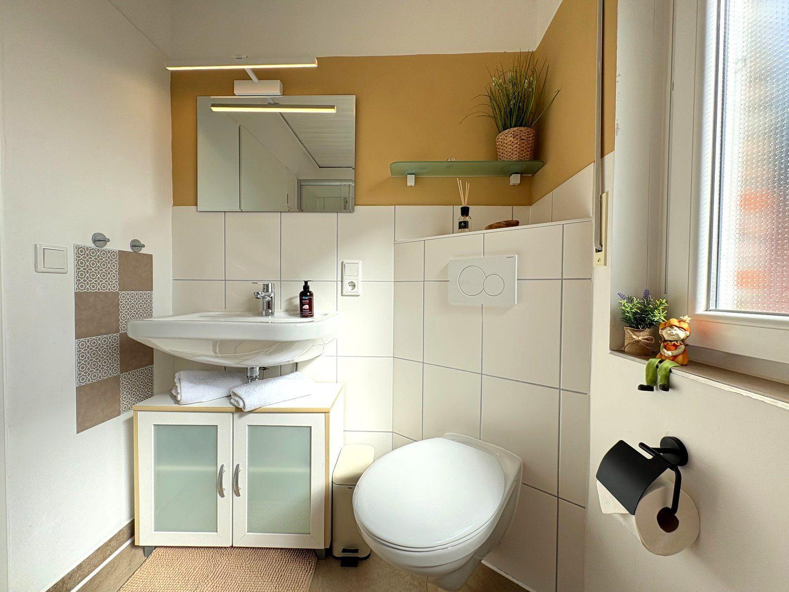 Badezimmer mit Waschbecken, Spiegel, Toilette und Fenster
