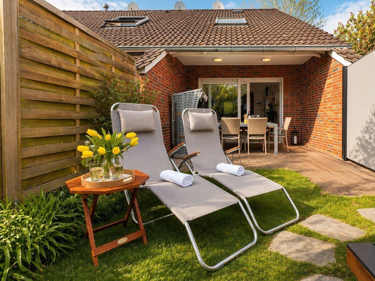 Zwei Liegestühle mit Handtuch und Tulpen auf grünem Rasen vor einer Terrasse.