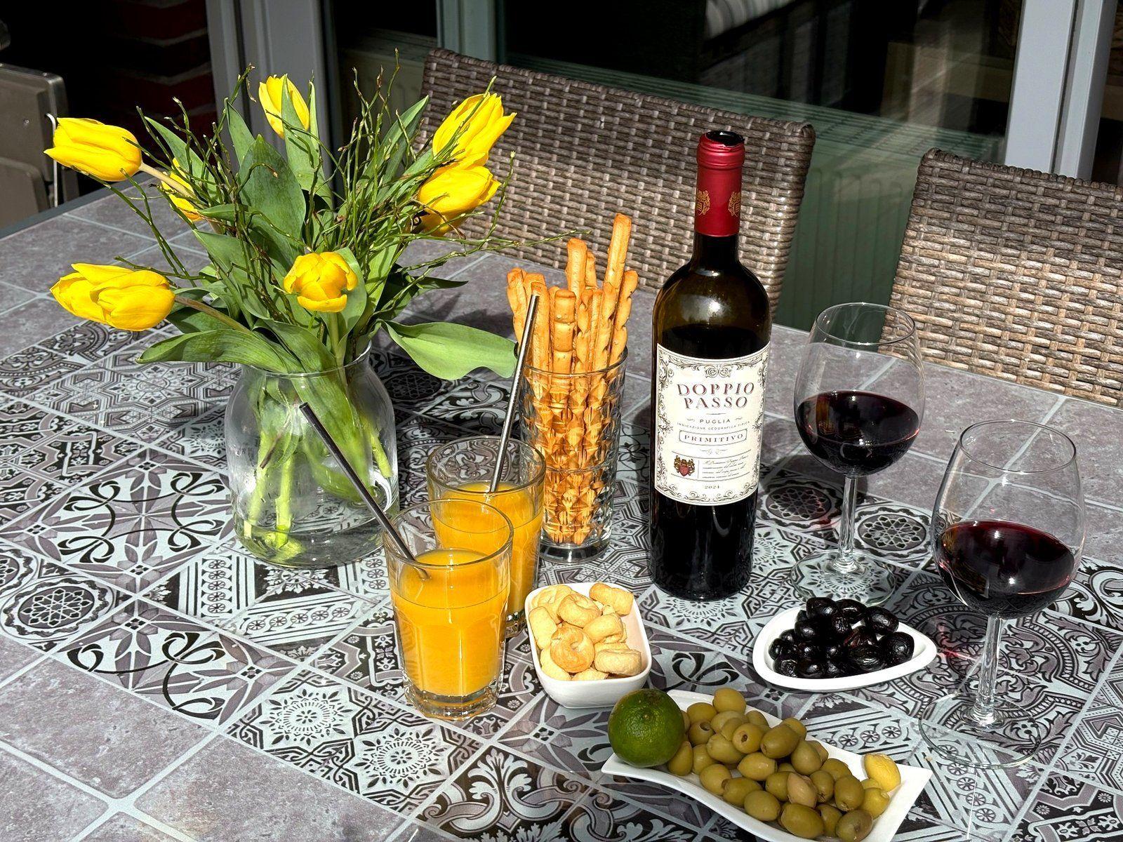 Tisch mit Wein, Orangensaft, Oliven und Tulpen auf einer Mosaikplatte.