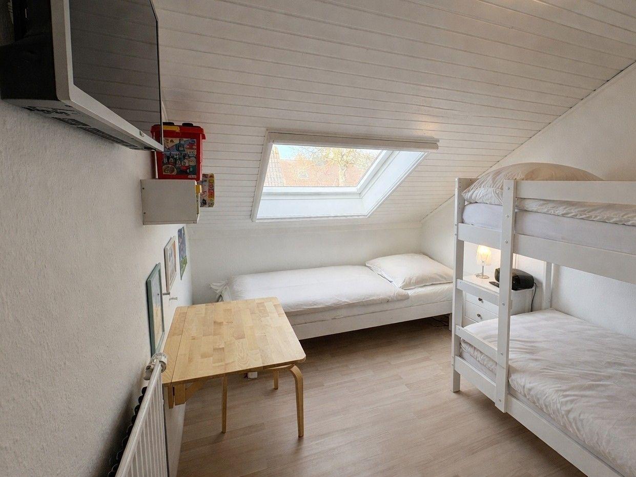 Zimmer mit Doppelstockbett, Einzelbett, Tisch und Dachfenster.