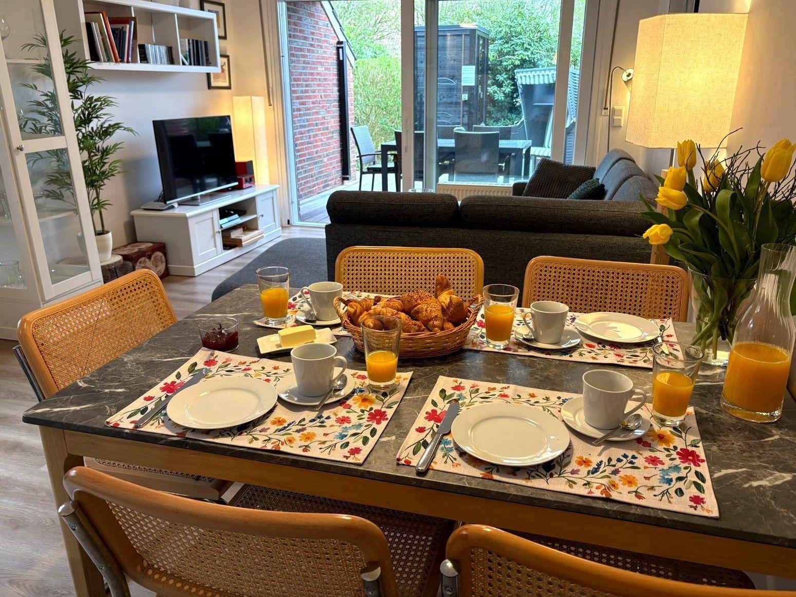 Frühstückstablett mit Kaffeetassen, Orangensaft und Croissants auf einem Esstisch.