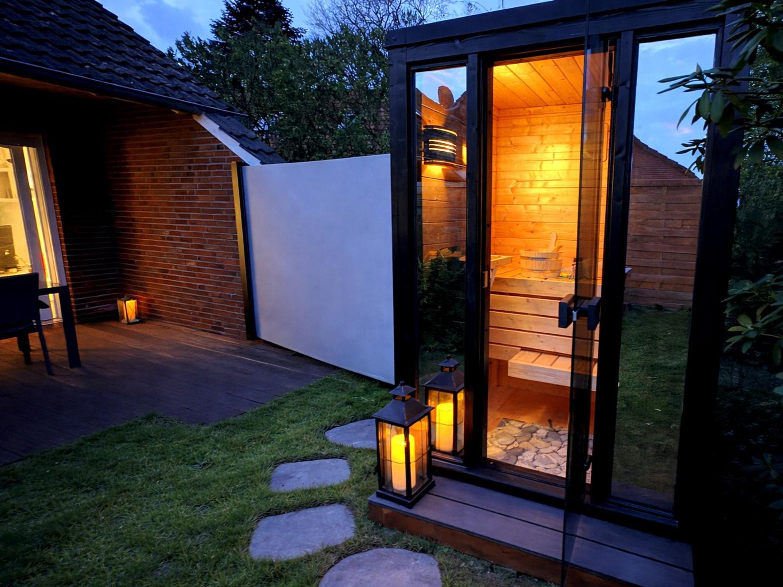 Außenliegende Sauna mit Holzwand und Glasfront. Beleuchtet durch Laterne und Innenbeleuchtung.