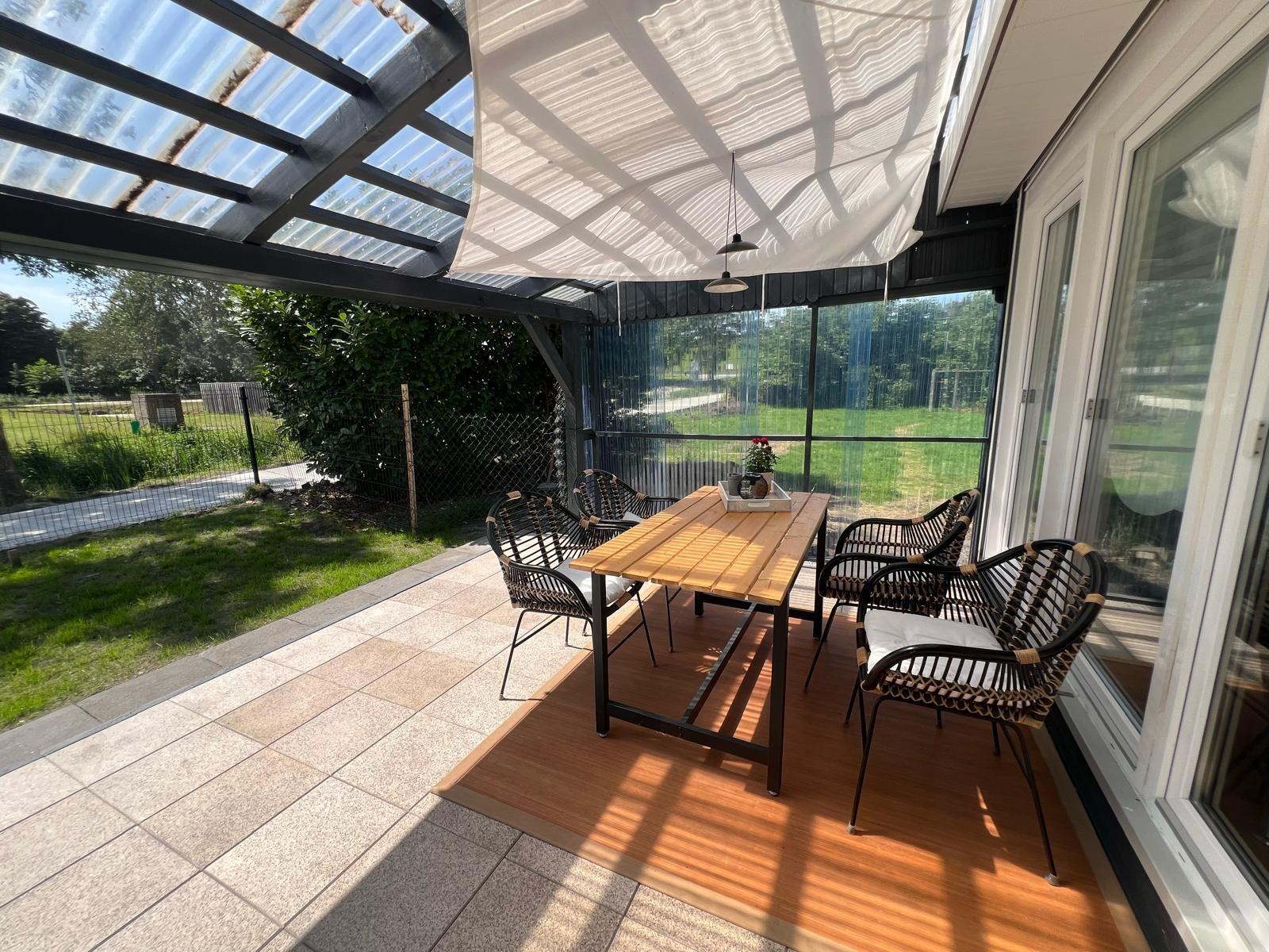 Terrasse mit Tisch und Stühlen unter Schutzdach und Sonnensegel.