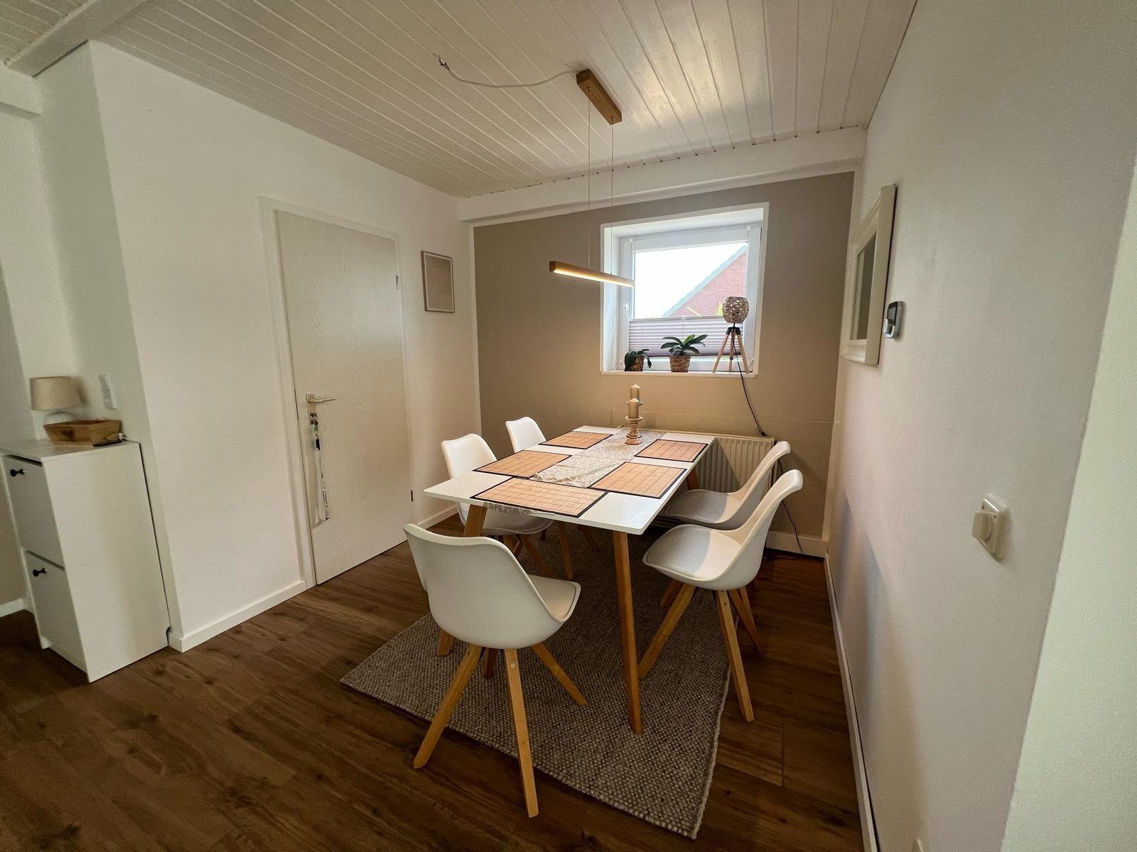 Esszimmer mit Tisch, Stühlen und Fenster. Holzboden und weiße Wände.