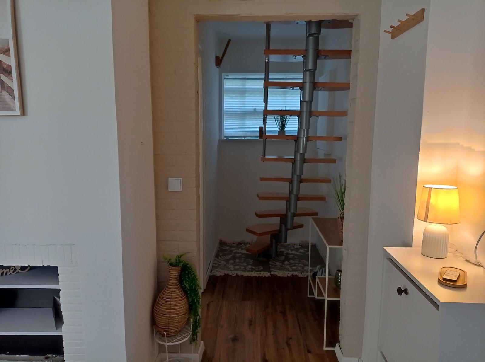 Durchgang mit Schraubenleiter zu oberem Stockwerk, Holzboden und kleiner Pflanze.