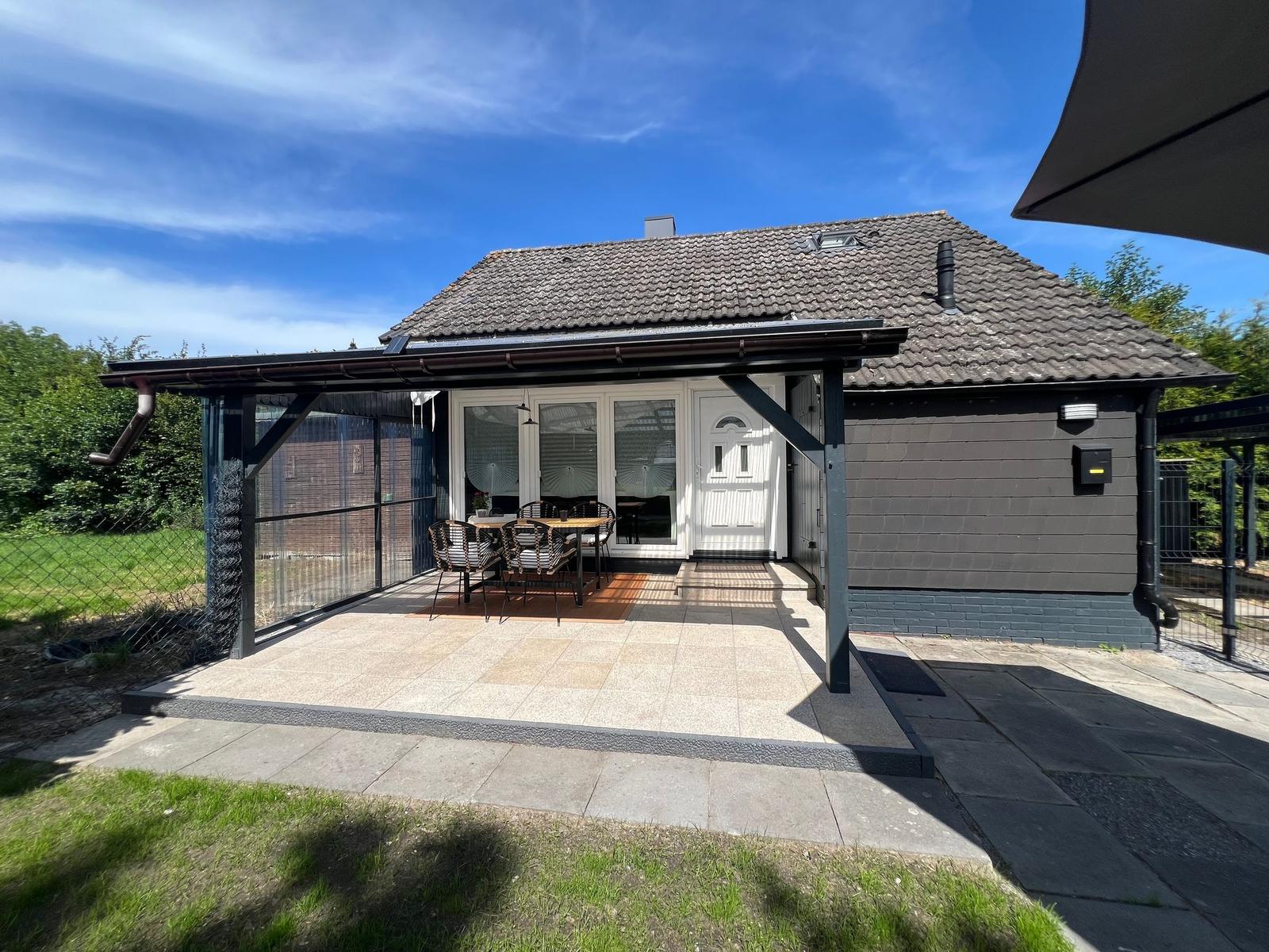 Haus mit Terrasse, Garten und Sitzgruppe unter Sonnenschutz.