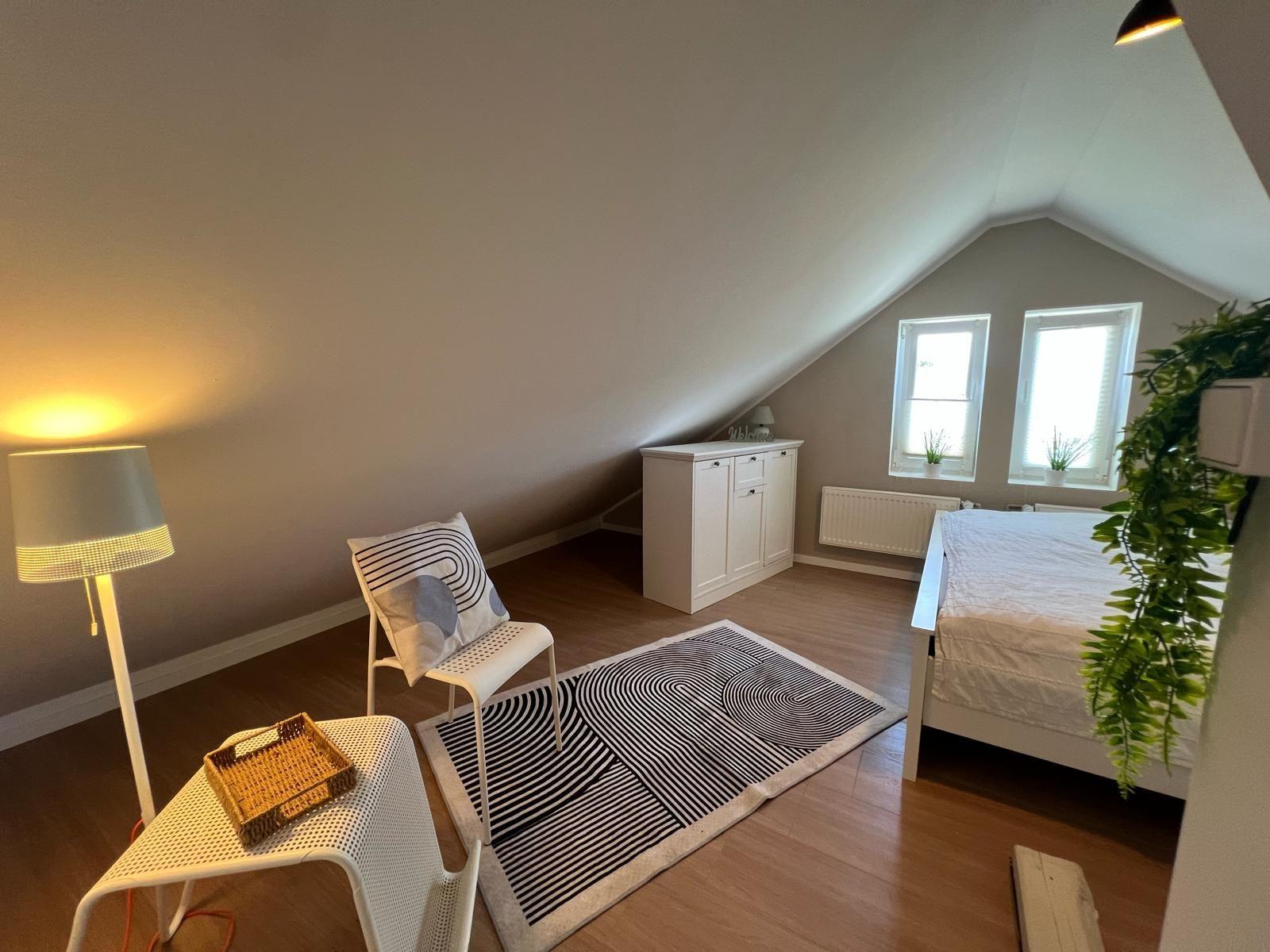 Schlafzimmer mit Dachschräge, Bett, Schrank und zwei Fenstern.