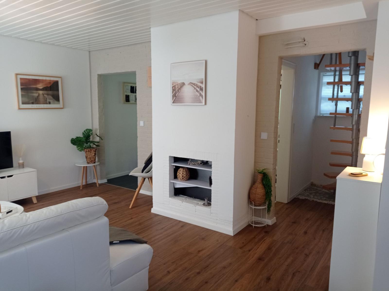 Wohnzimmer mit weißem Sofa, Kamin und Holzboden. Treppe führt zur oberen Etage.