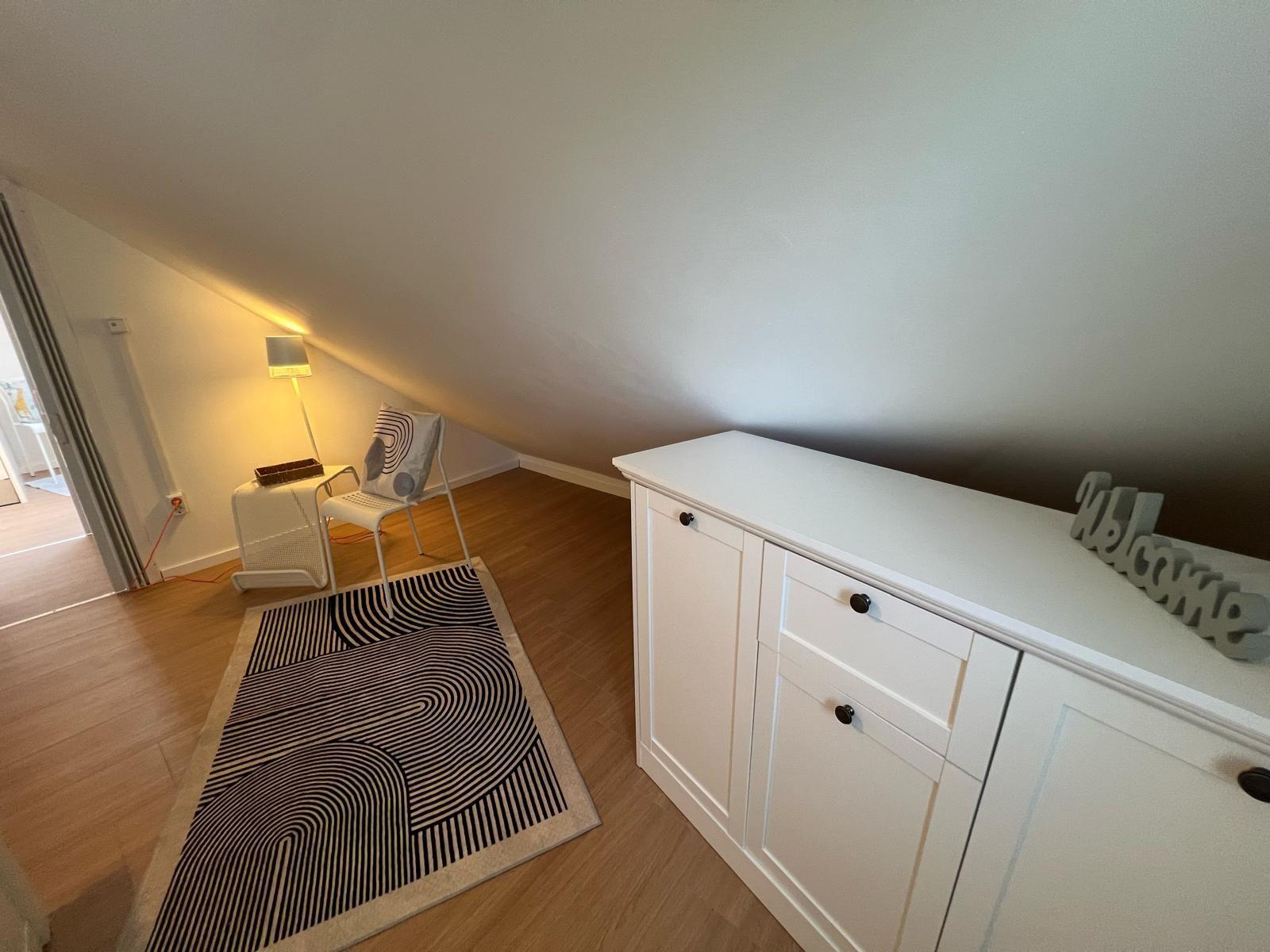 Schlafzimmer mit Dachschräge, weißem Schrank und gemustertem Teppich.