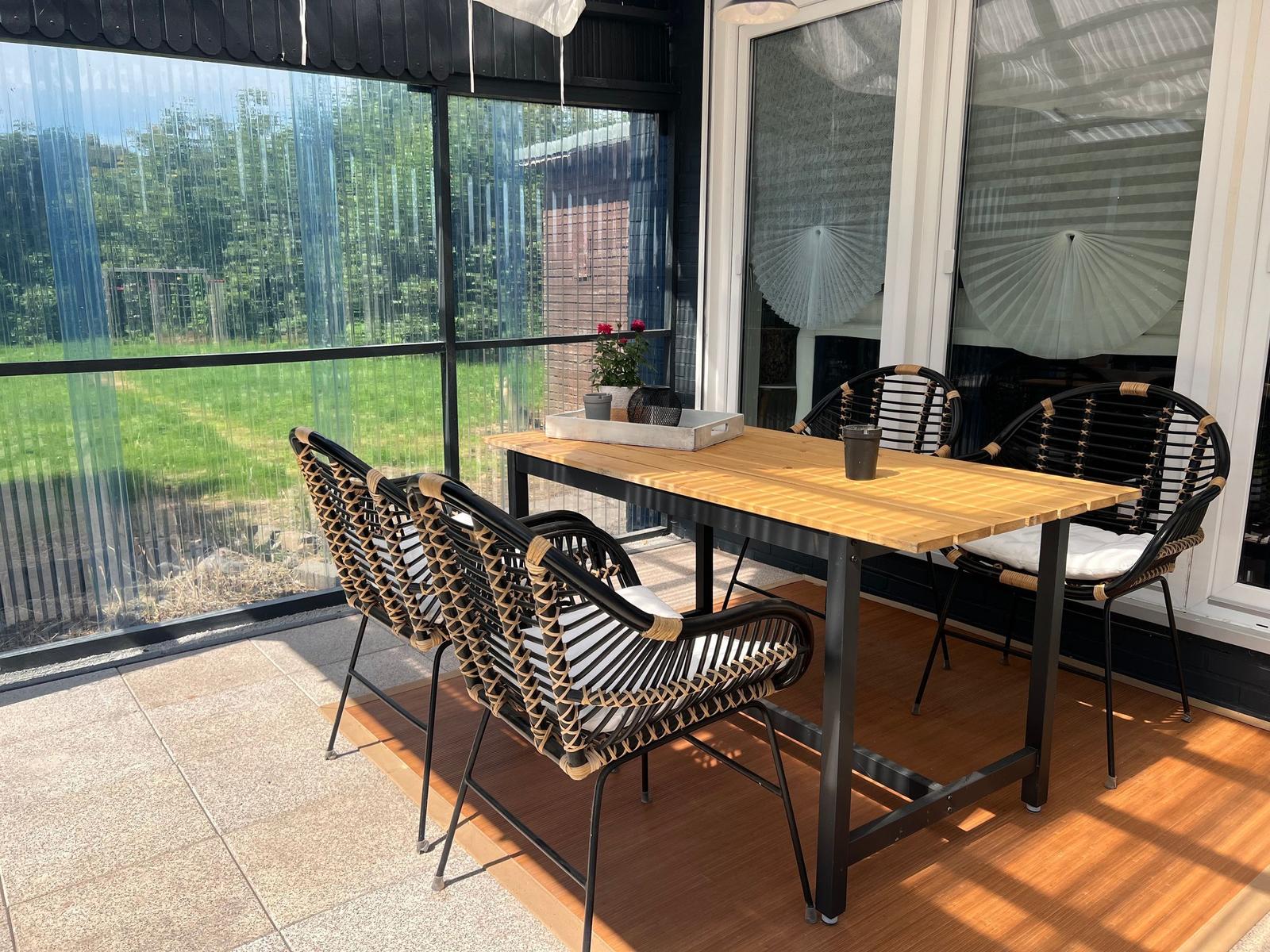 Terrasse mit Tisch und vier Stühlen, Blick auf grünen Garten.