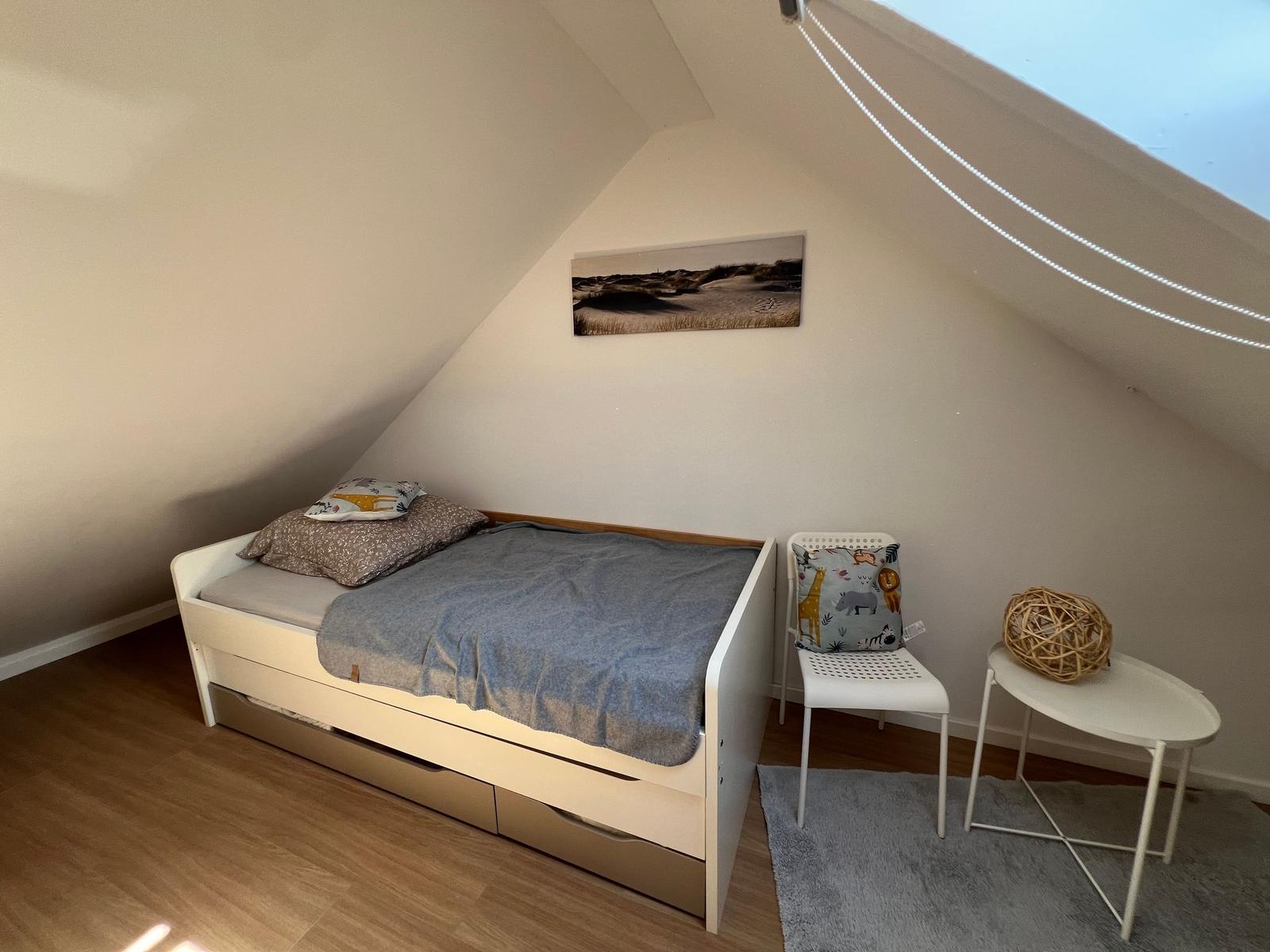 Schlafzimmer mit Dachschrägen, Bett, Stuhl und Tisch.
