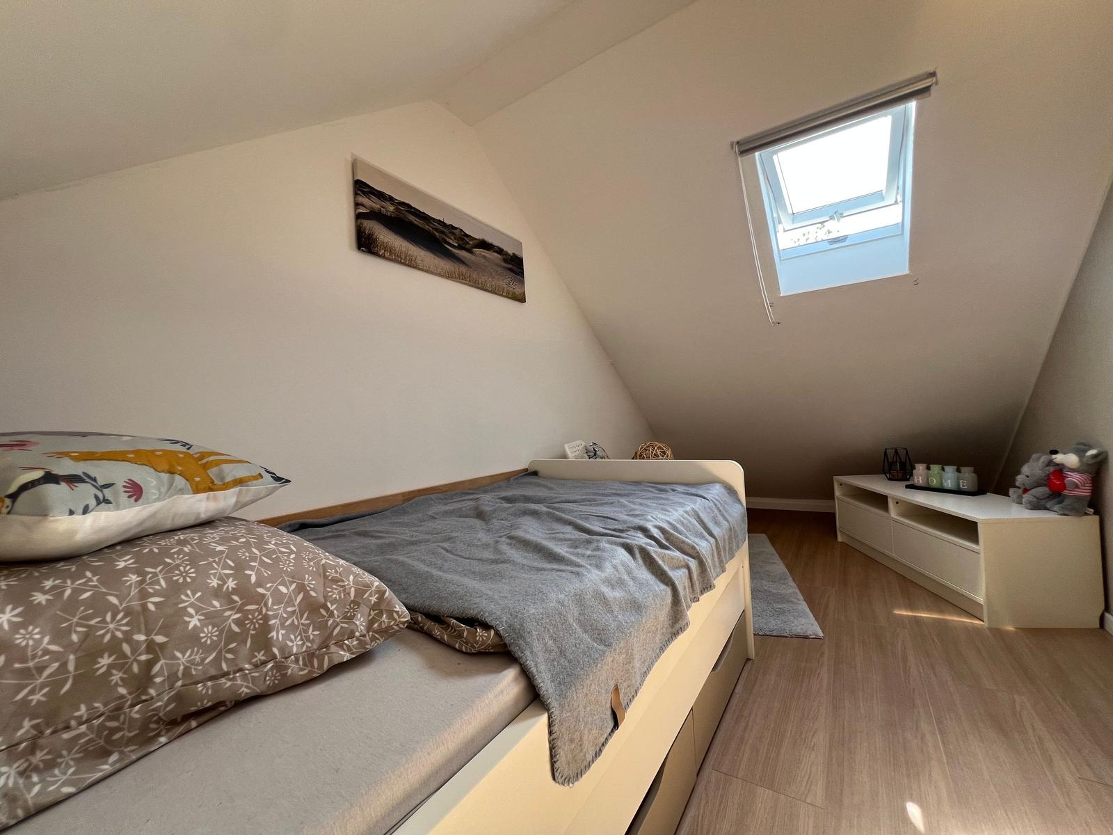 Schlafzimmer mit Dachschräge, Bett, Fenster und Schrank.