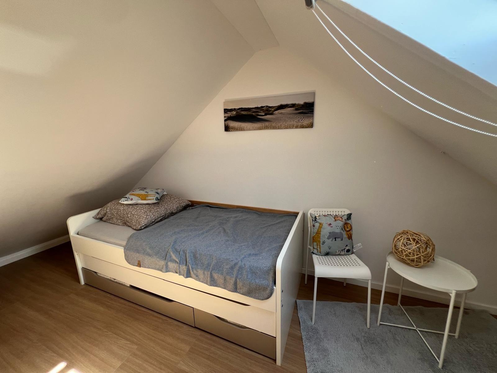 Schlafzimmer mit Dachschräge, Bett, Stuhl und Tisch.