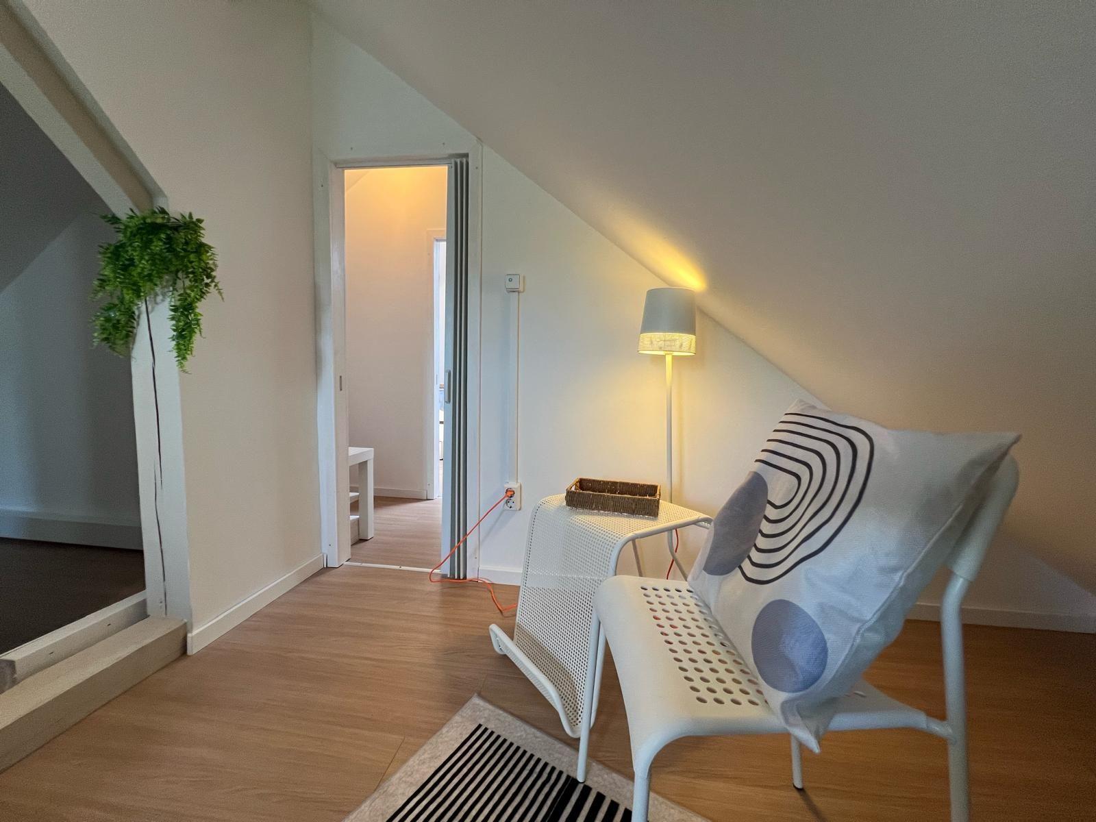 Dachbodenwohnung mit Sitzgelegenheit, Stehlampe und Pflanze.