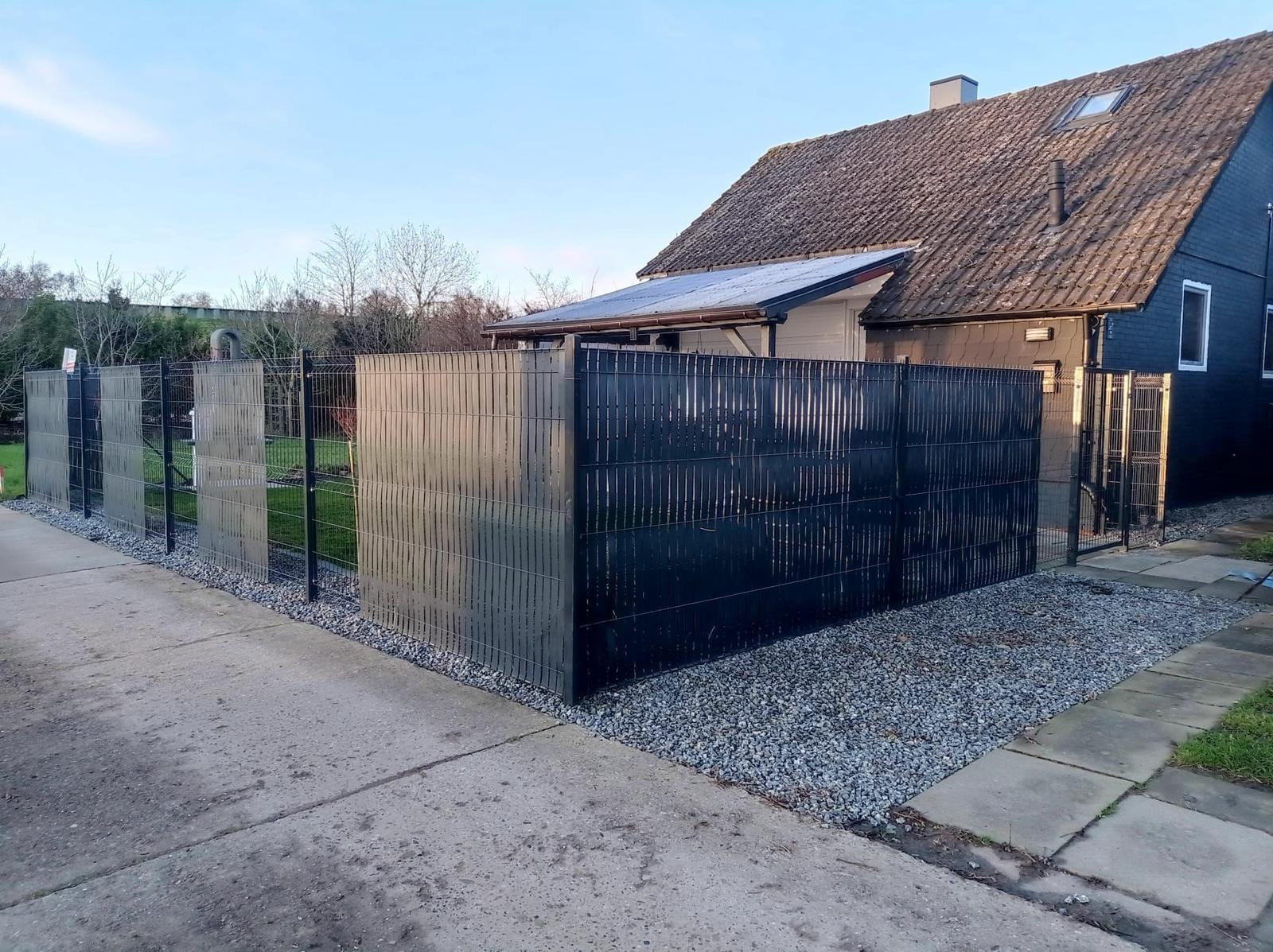 Hinterhof mit Zaun, Kies und Garage neben Haus.
