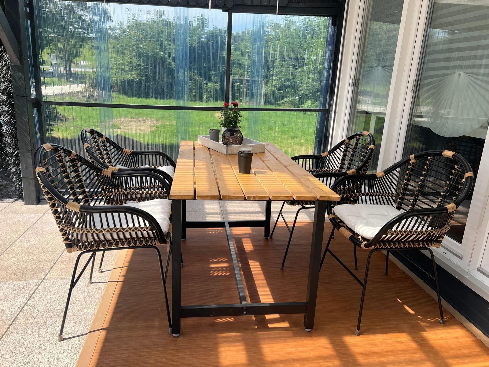 Terrasse mit Holztisch und sechs Stühlen, Blick auf grünen Garten.