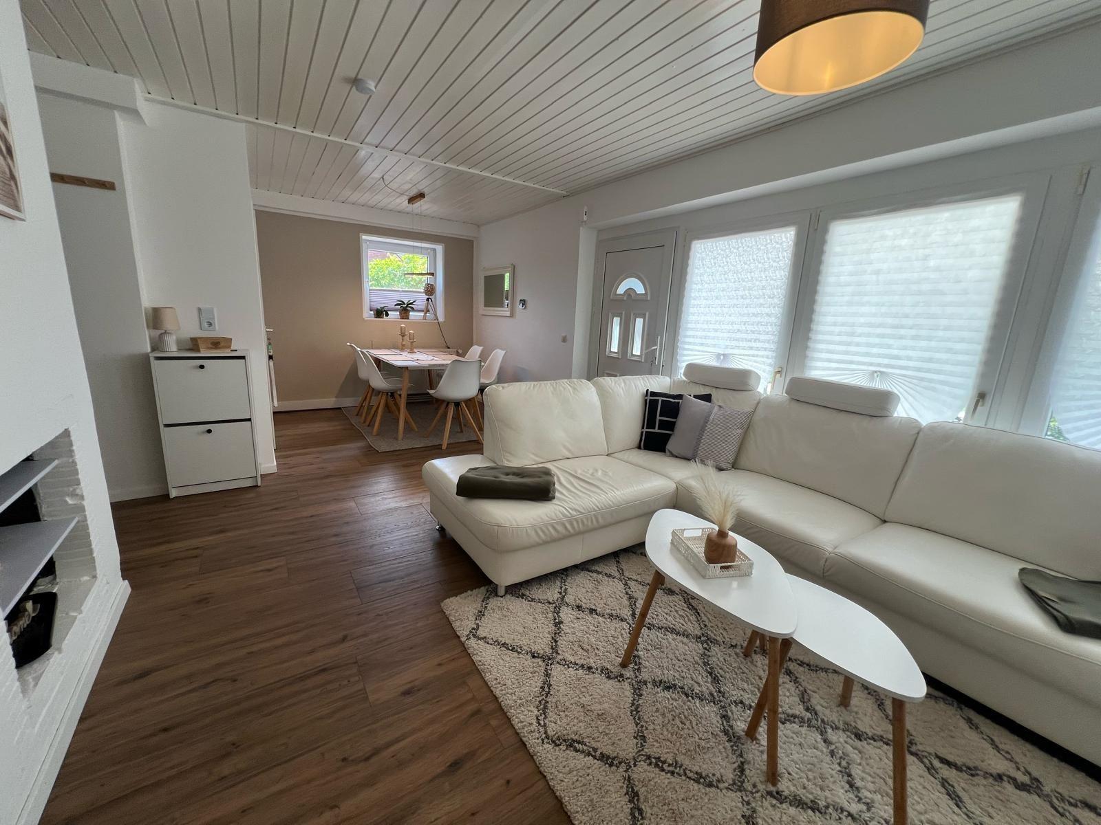 Wohnzimmer mit weißem Sofa, Holzboden und Fenstern mit Jalousien.