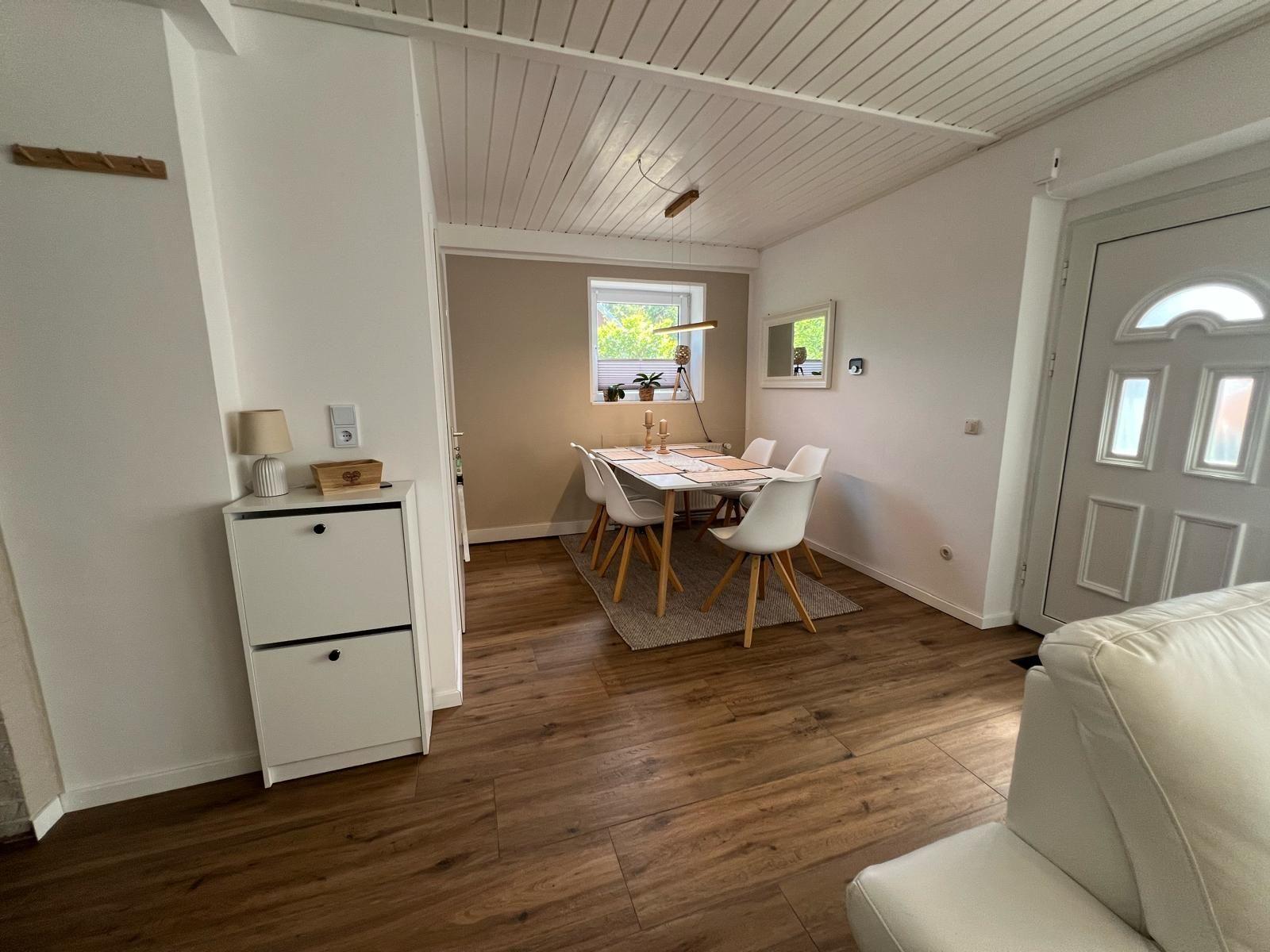 Esszimmer mit Tisch, Stühlen und Fenster. Holzboden und weiße Wände.