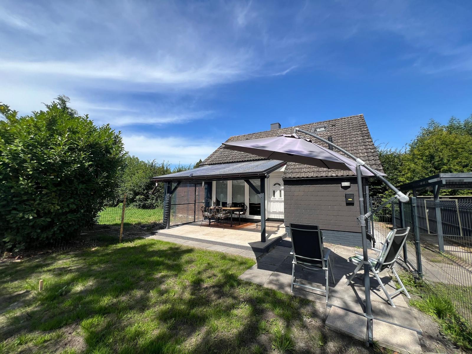 Haus mit Terrasse, Sitzgelegenheiten und Sonnenschirm im Garten