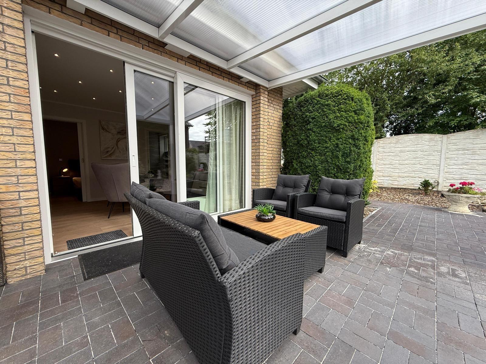 Terrasse mit Sitzgruppe unter Überdachung, Zugang ins Haus durch Schiebetür.