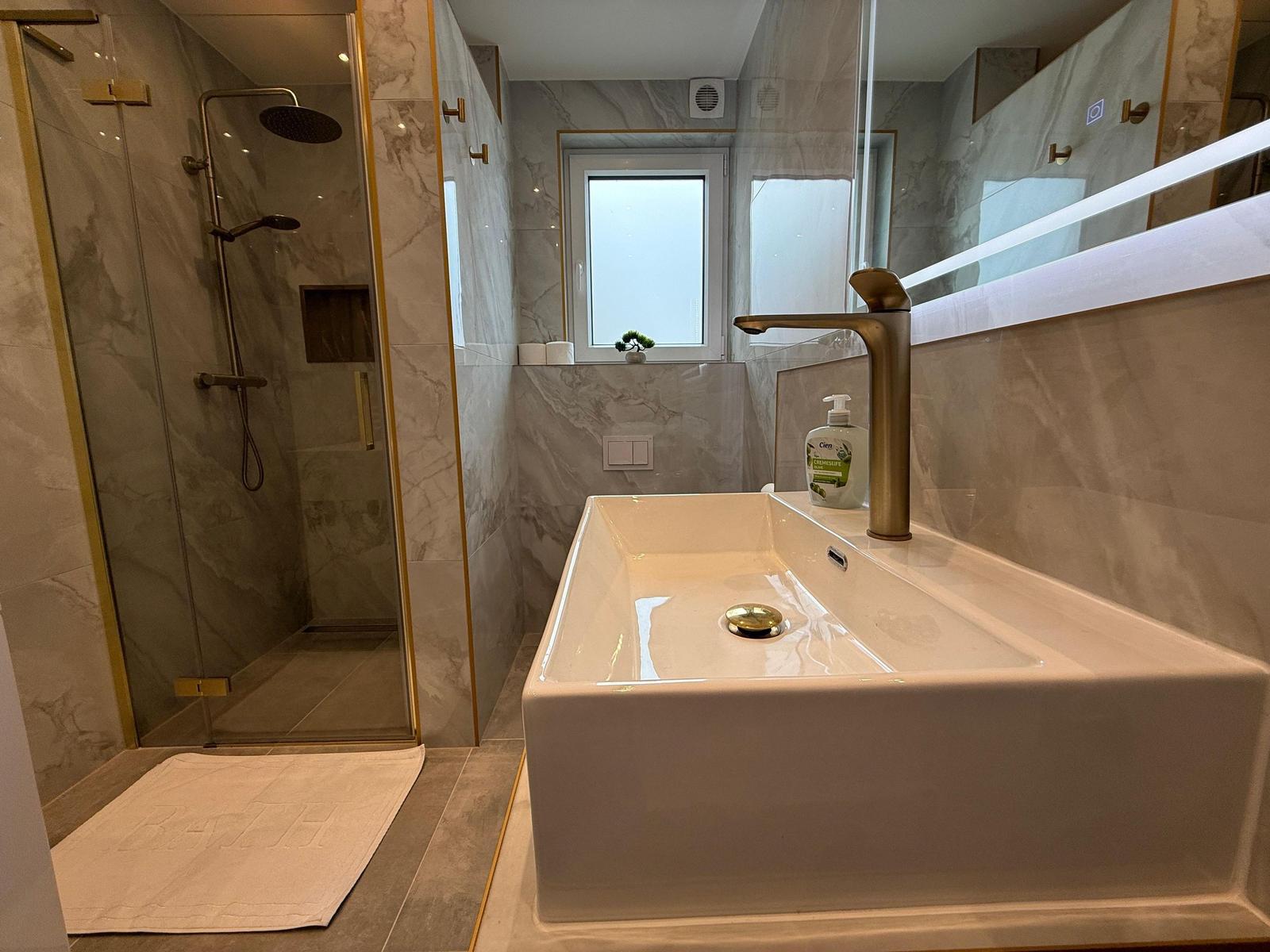 Badezimmer mit Dusche, Waschbecken und Fenster.