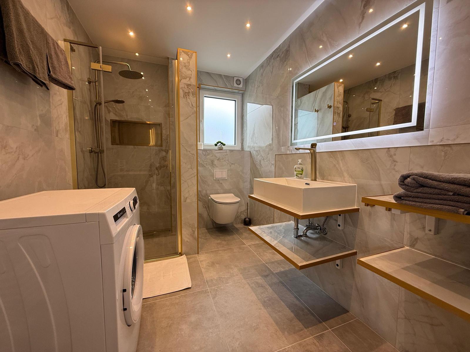 Badezimmer mit Dusche, Waschmaschine und Spiegel