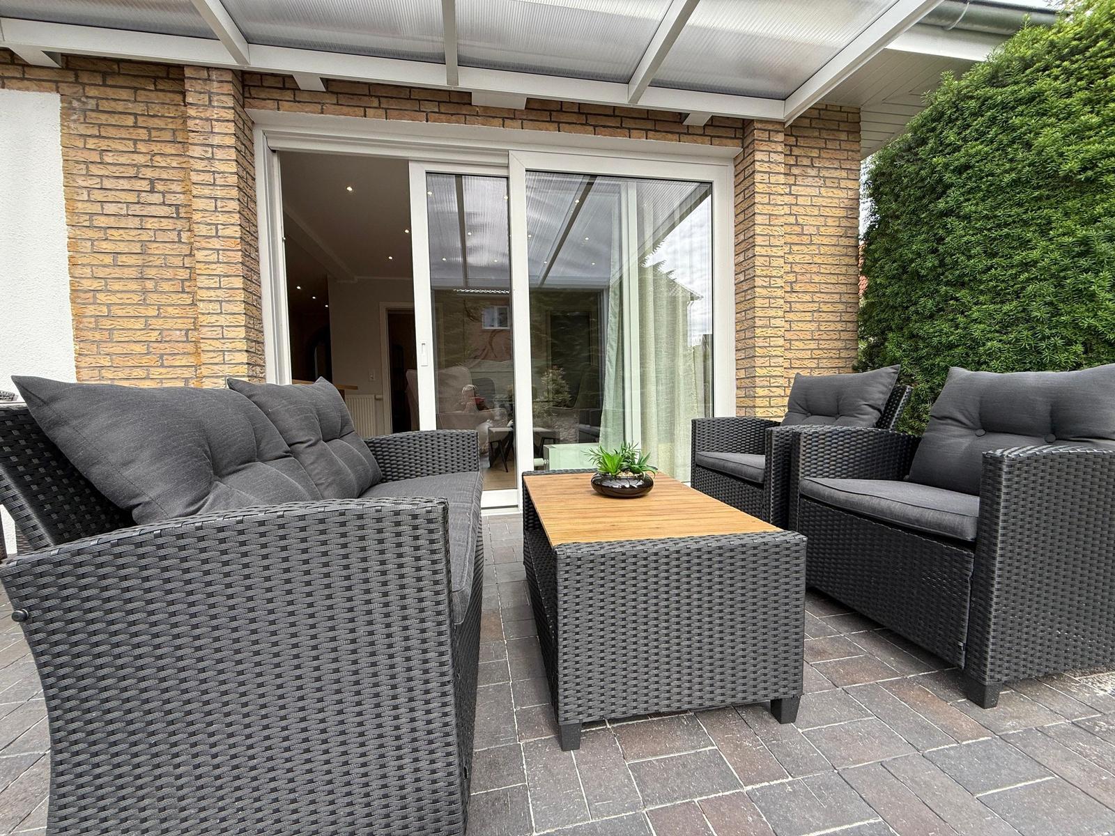Terrasse mit grauem Rattan-Sofa, zwei Sesseln und Tisch unter Dach.