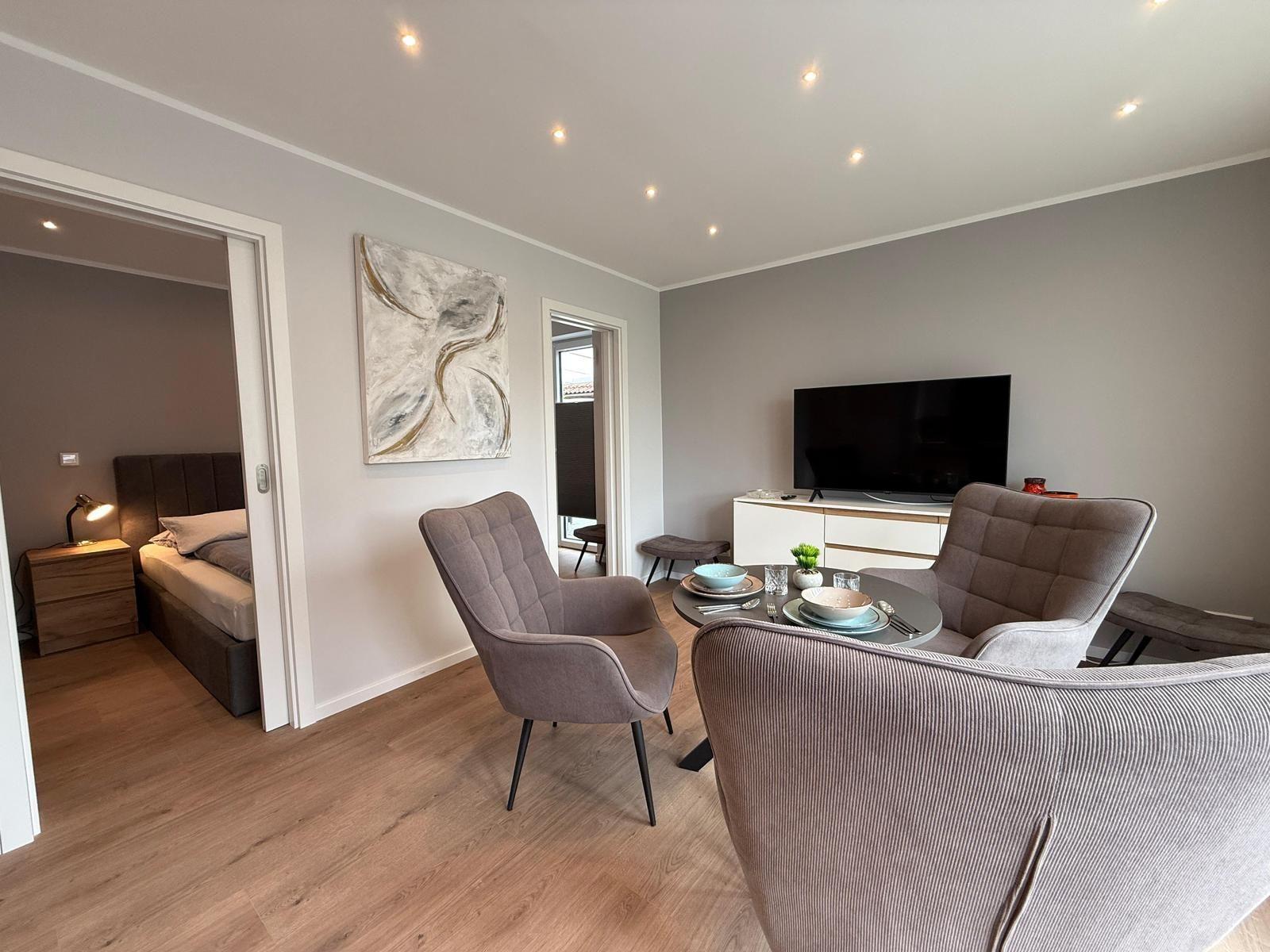 Wohnzimmer mit Sitzgelegenheit, Fernseher und Blick in Schlafzimmer.