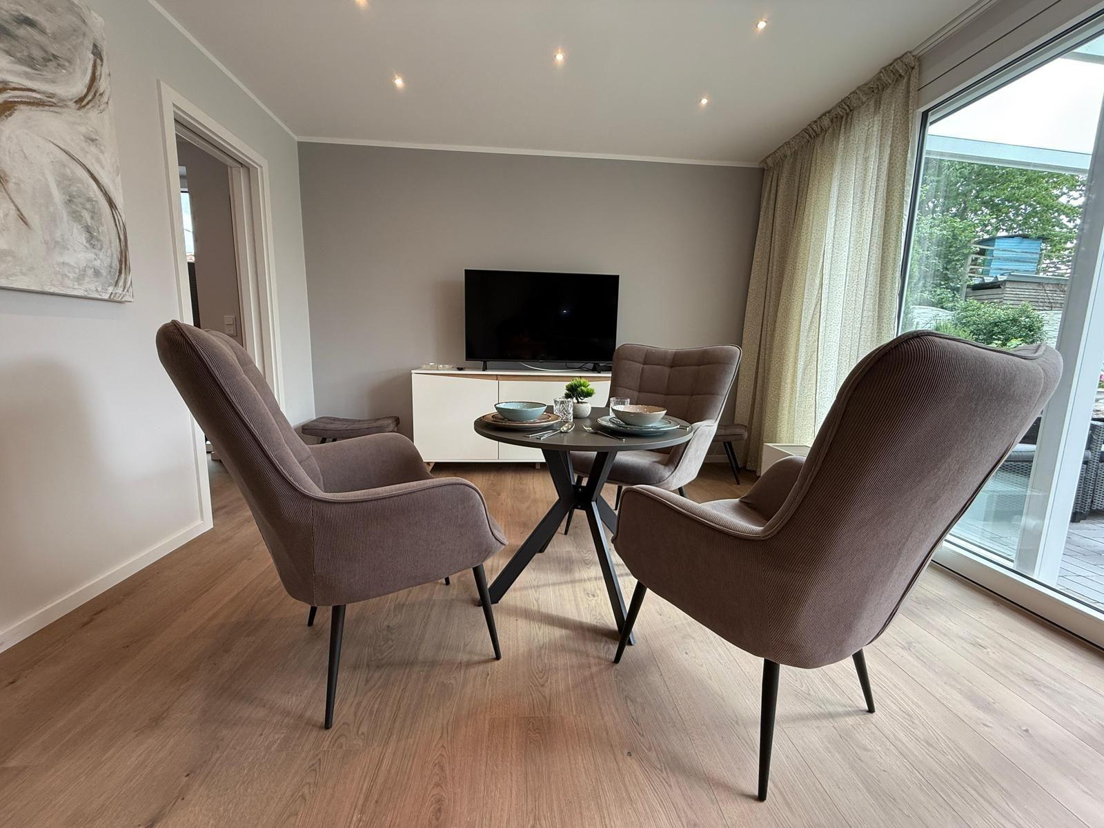 Essbereich mit runden Tisch und vier Stühlen, Fernseher und großes Fenster.