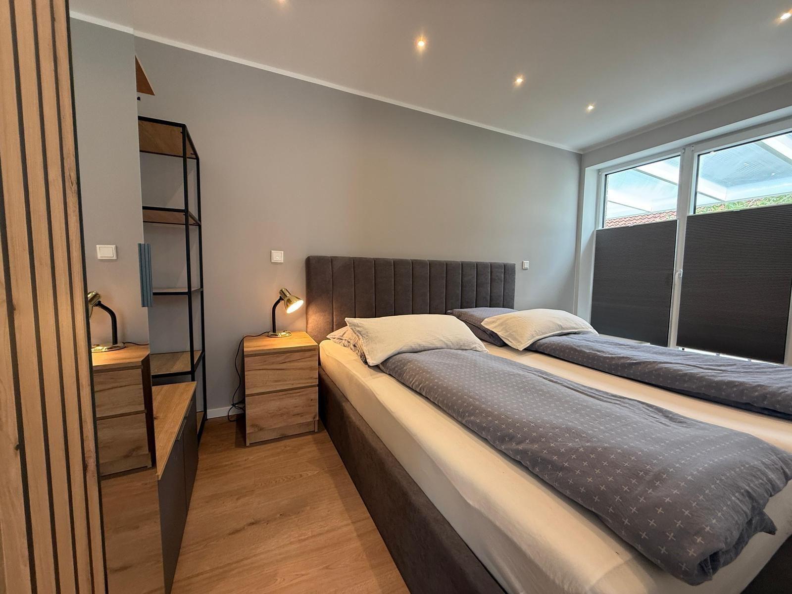 Schlafzimmer mit Doppelbett, Nachttisch und Schrank. Fenster mit Jalousie.