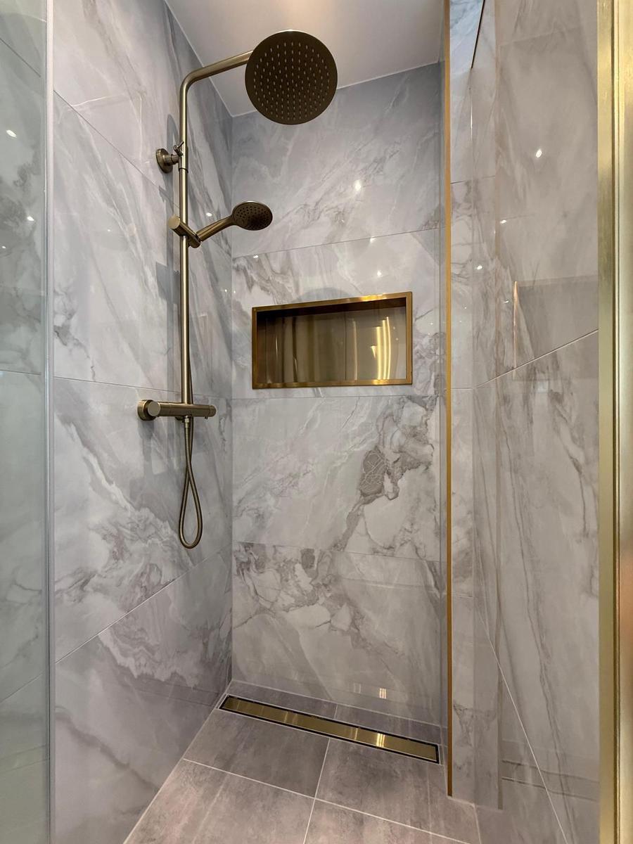 Dusche mit marblen Wänden und goldfarbenen Armaturen und Ablage