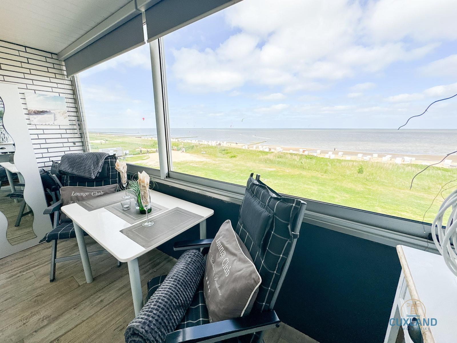 Terrasse mit Tisch und Stühlen. Blick auf Strand und Meer.