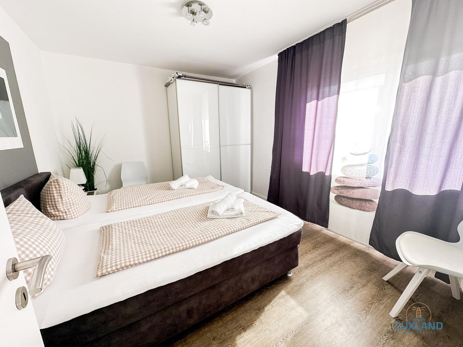Schlafzimmer mit Doppelbett, Schwebetüren und Vorhängen mit Steinmotiv.