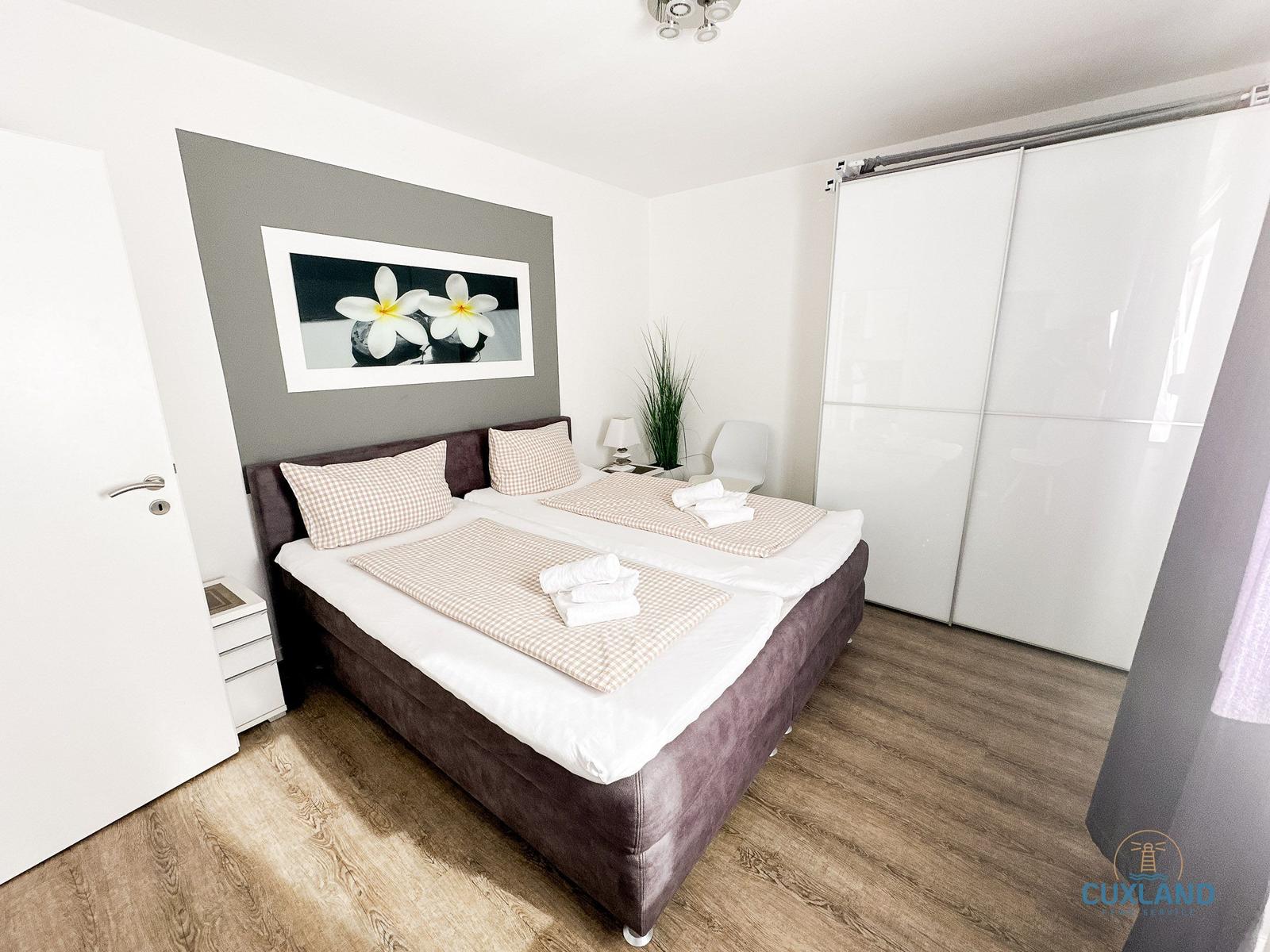Schlafzimmer mit Doppelbett, Schwebetüren und Wandbild mit Blumen.