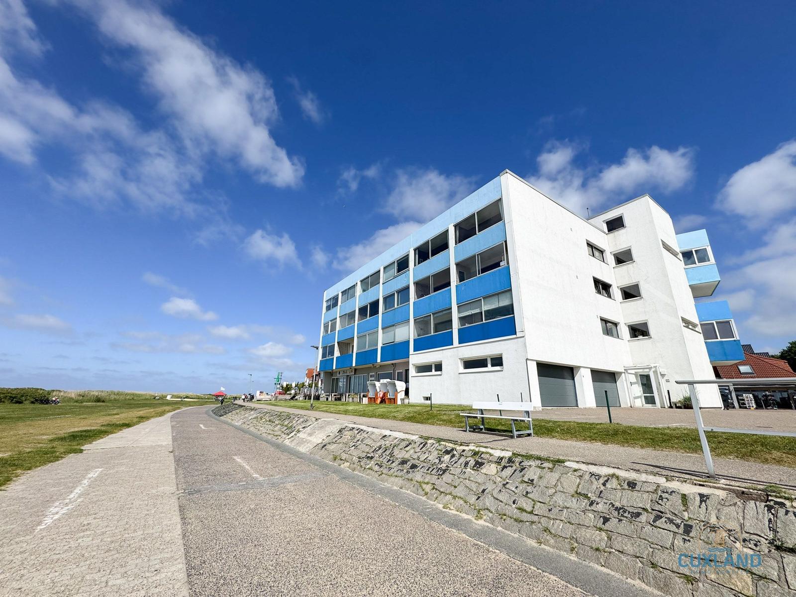 Moderne Wohnanlage mit blauen Balkonen und weißer Fassade an Strandpromenade.