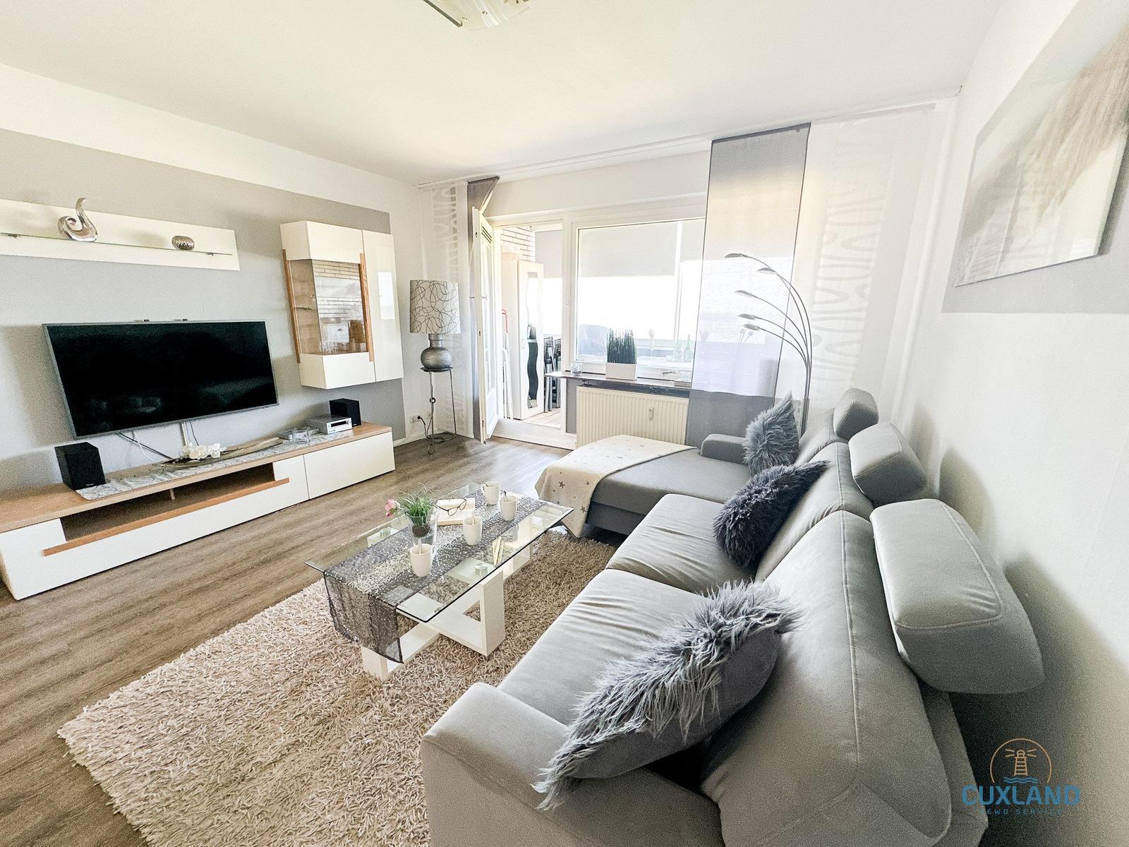 Wohnzimmer mit Sofa, Fernseher und Glas-Tisch. Fenster mit Blick nach draußen.