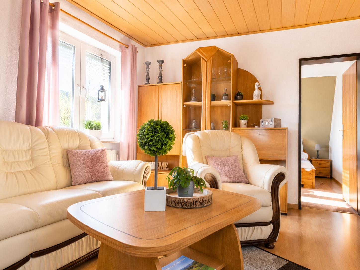Wohnzimmer mit Sofa, Sessel, Tisch und Holzmöbel. Durchgang zur Schlafzimmer.