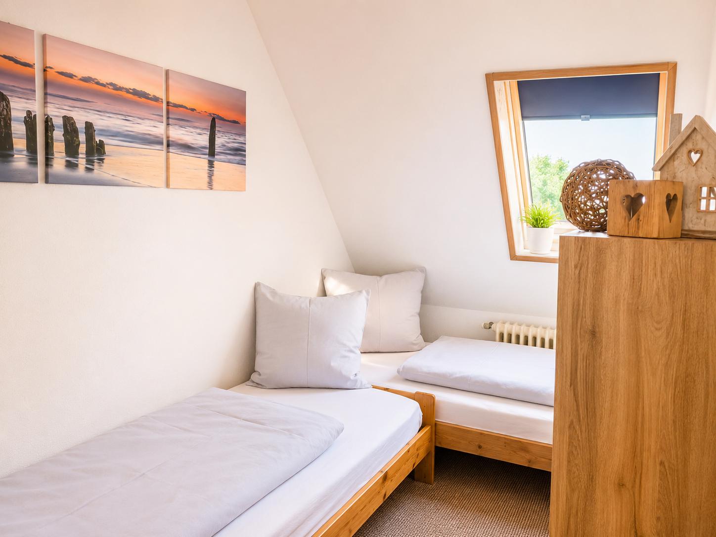 Zwei Betten in einem Dachzimmer mit Fenster und Wandbildern.