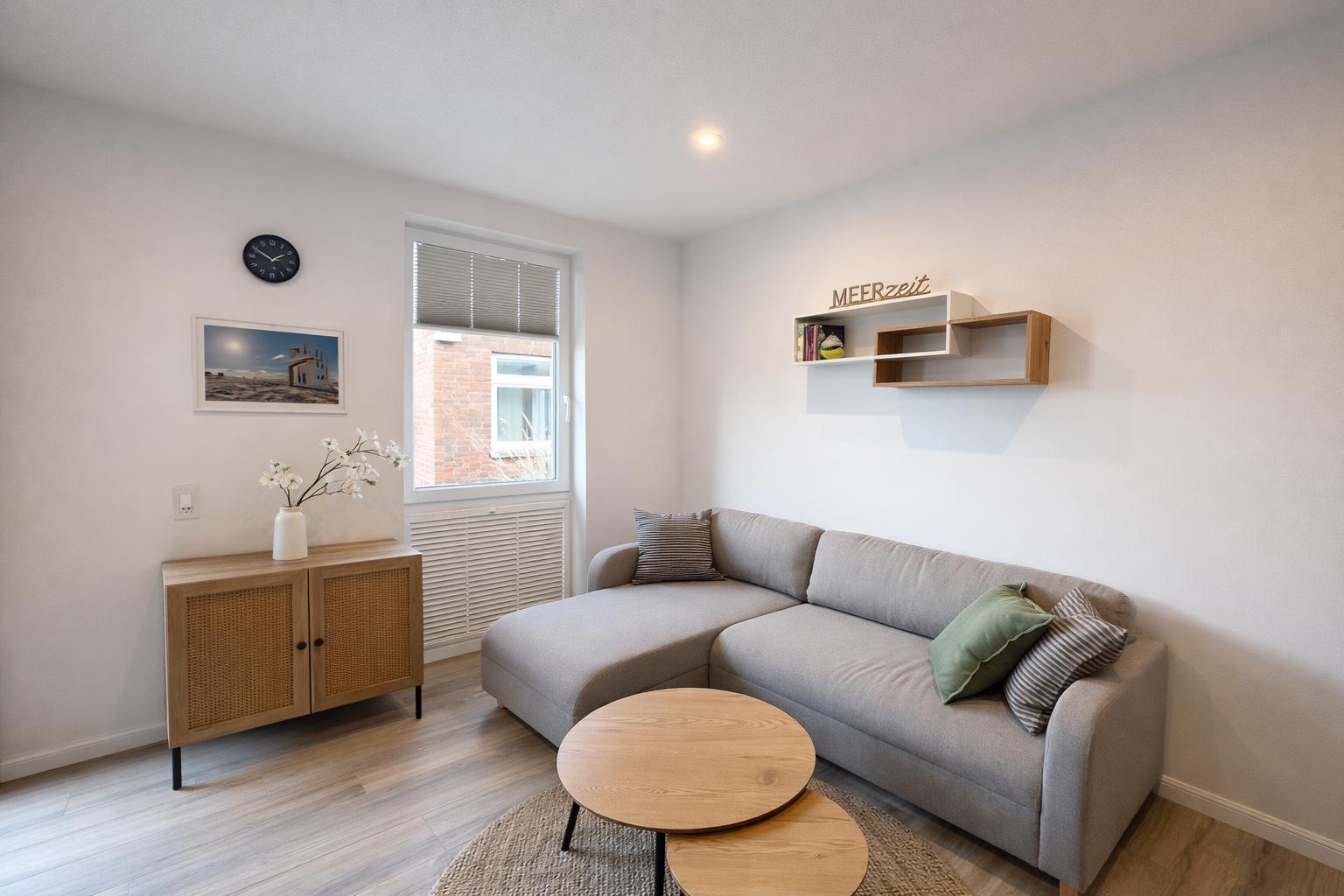 Ein Wohnzimmer mit grauem Sofa, runden Holztischen und einer Wanduhr.