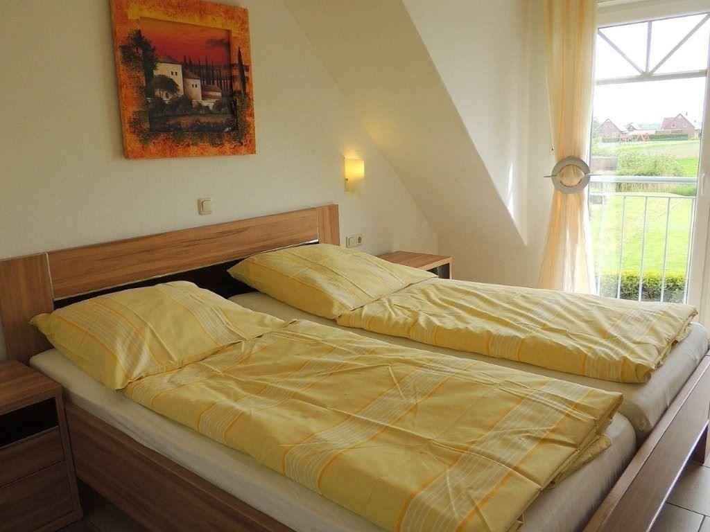 Zimmer mit Doppelbett, Holzgestell, Wandbild und Balkontür mit Blick auf Grünfläche.