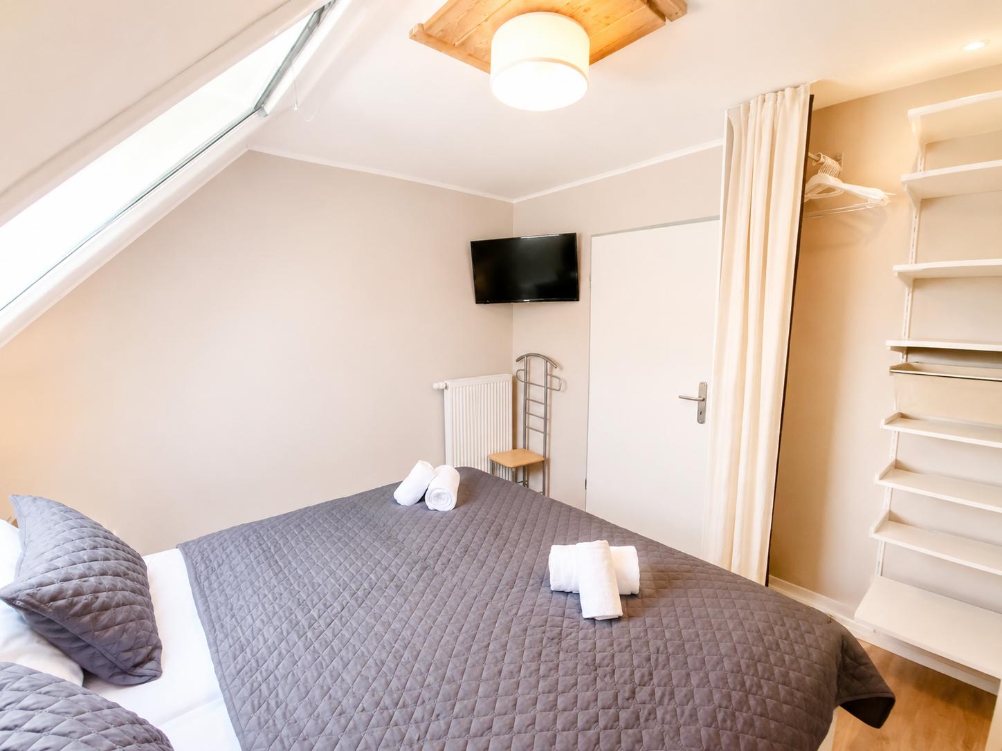 Schlafzimmer mit Dachfenster, Bett, TV und Kleiderschrank.