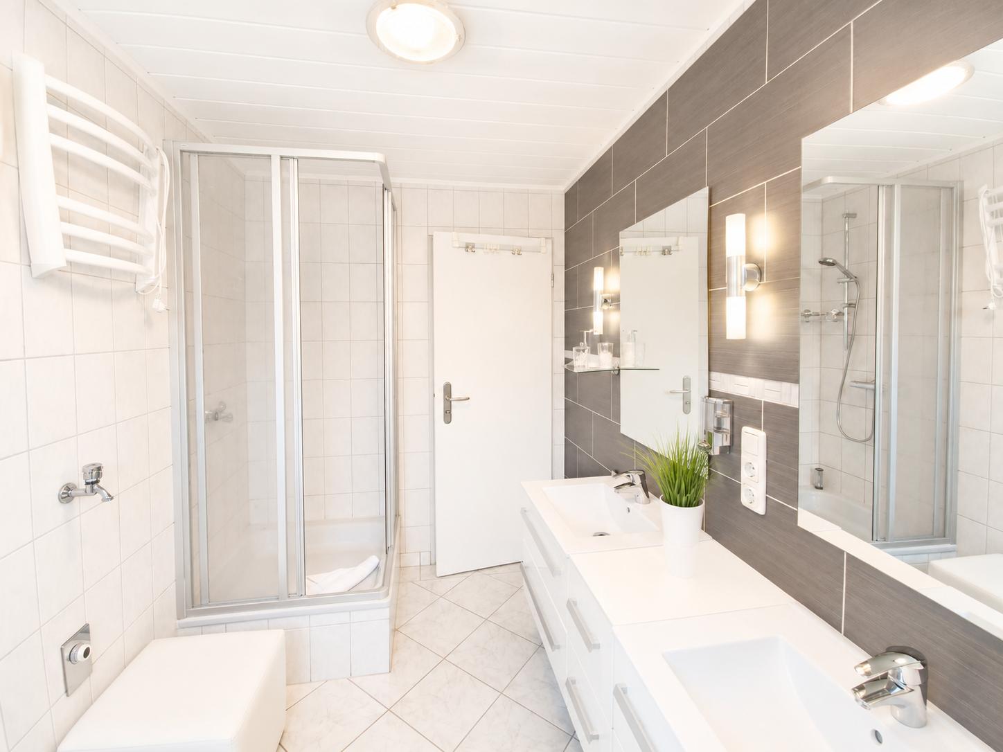 Badezimmer mit Dusche, Waschbecken und Toilette. Moderne Einrichtung mit Spiegel und Beleuchtung.