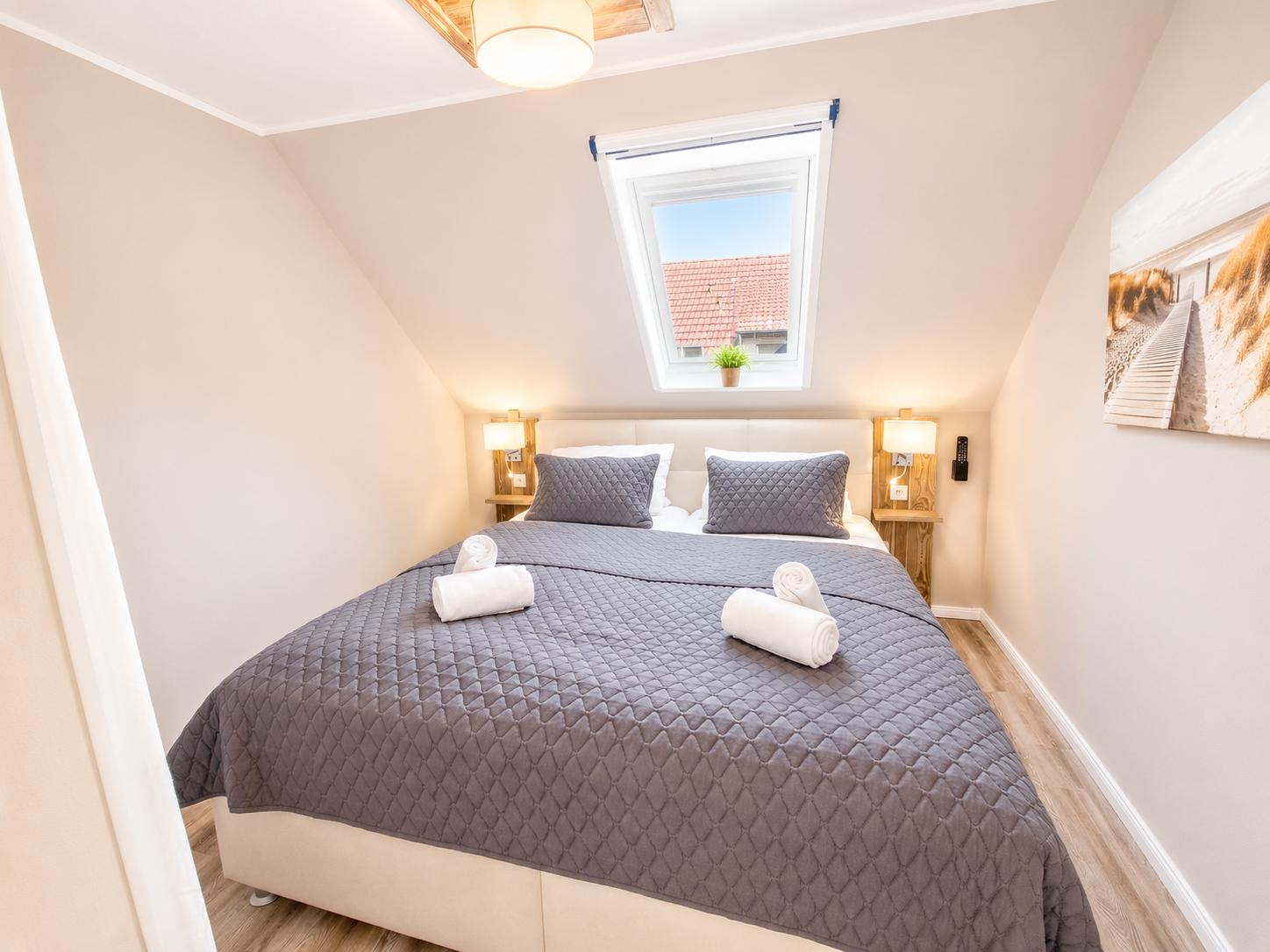 Schlafzimmer mit Dachfenster, Bett mit grauer Bettwäsche und Holzfußboden.