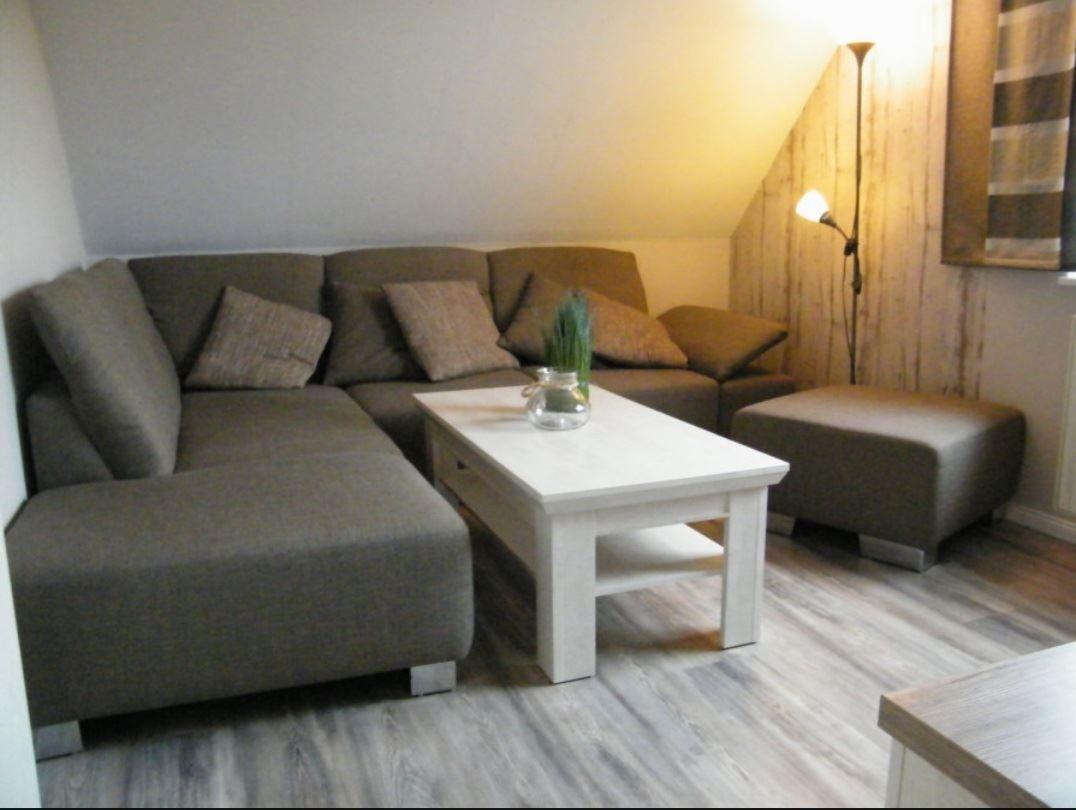 Ein Wohnzimmer mit grauem Sofa, weißem Tisch und Holzwand.