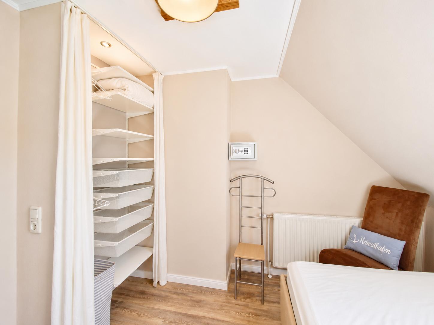 Schlafzimmer mit Kleiderschrank, Bett und Sessel. Dachschrägen und Holzboden.